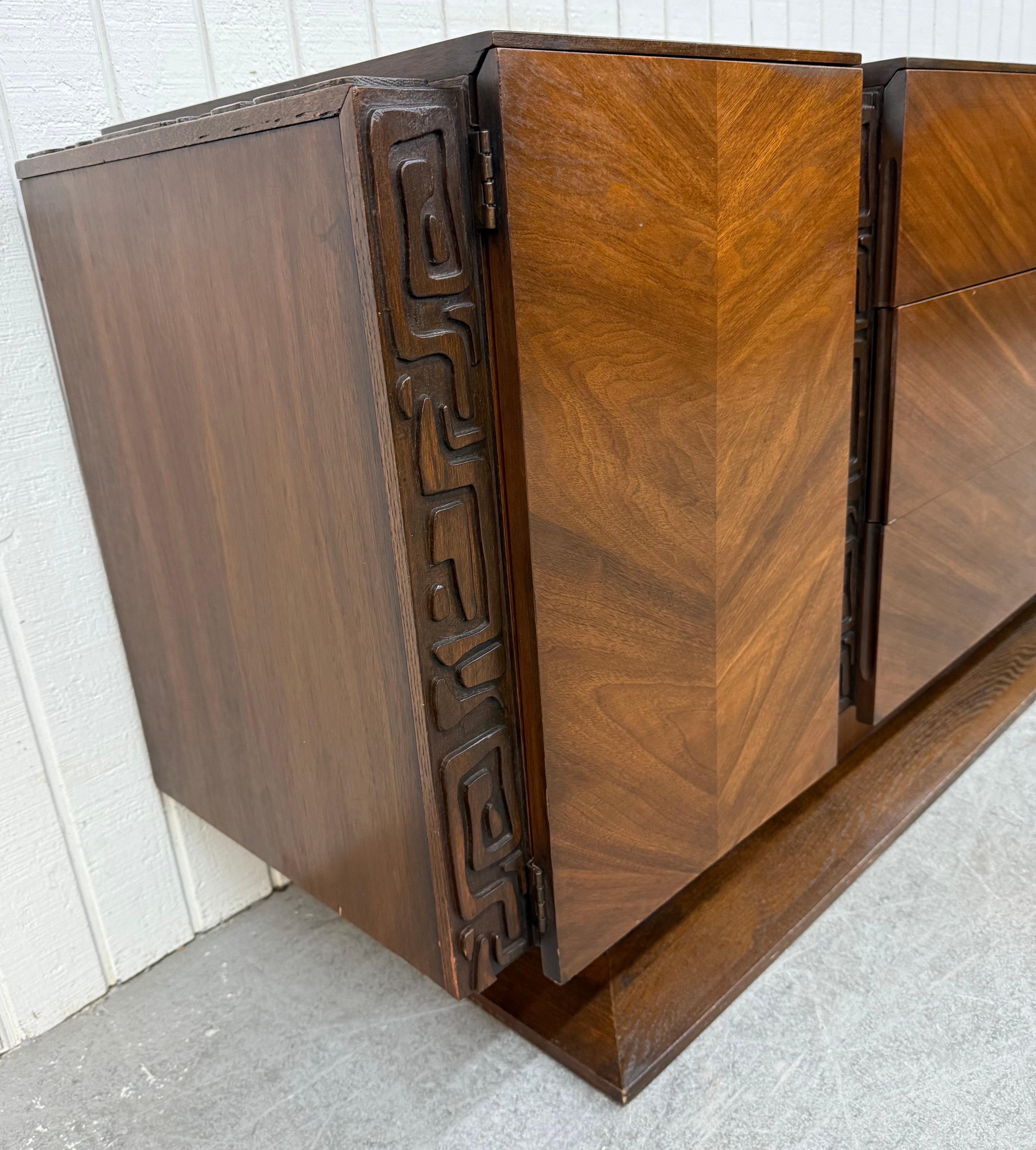 This listing is for a Mid-Century Modern United Tiki Walnut 9-Drawer Dresser. Featuring a straight line tiki style design, doors on each end that open up to hidden drawers, three larger center drawers, plinth base, and beautiful walnut finish. This