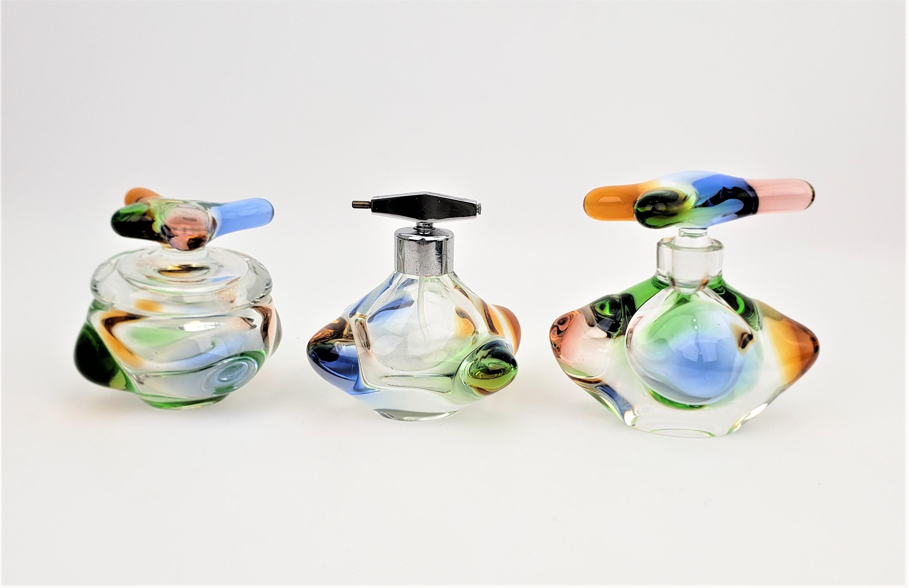 This Mid-Century Modern three piece art glass dresser set is unsigned, but done in the style of Val Saint Lambert of France in approximately 1960. The heavy multi-colored crystal perfume bottle and covered dresser jar have freeform stylized lids