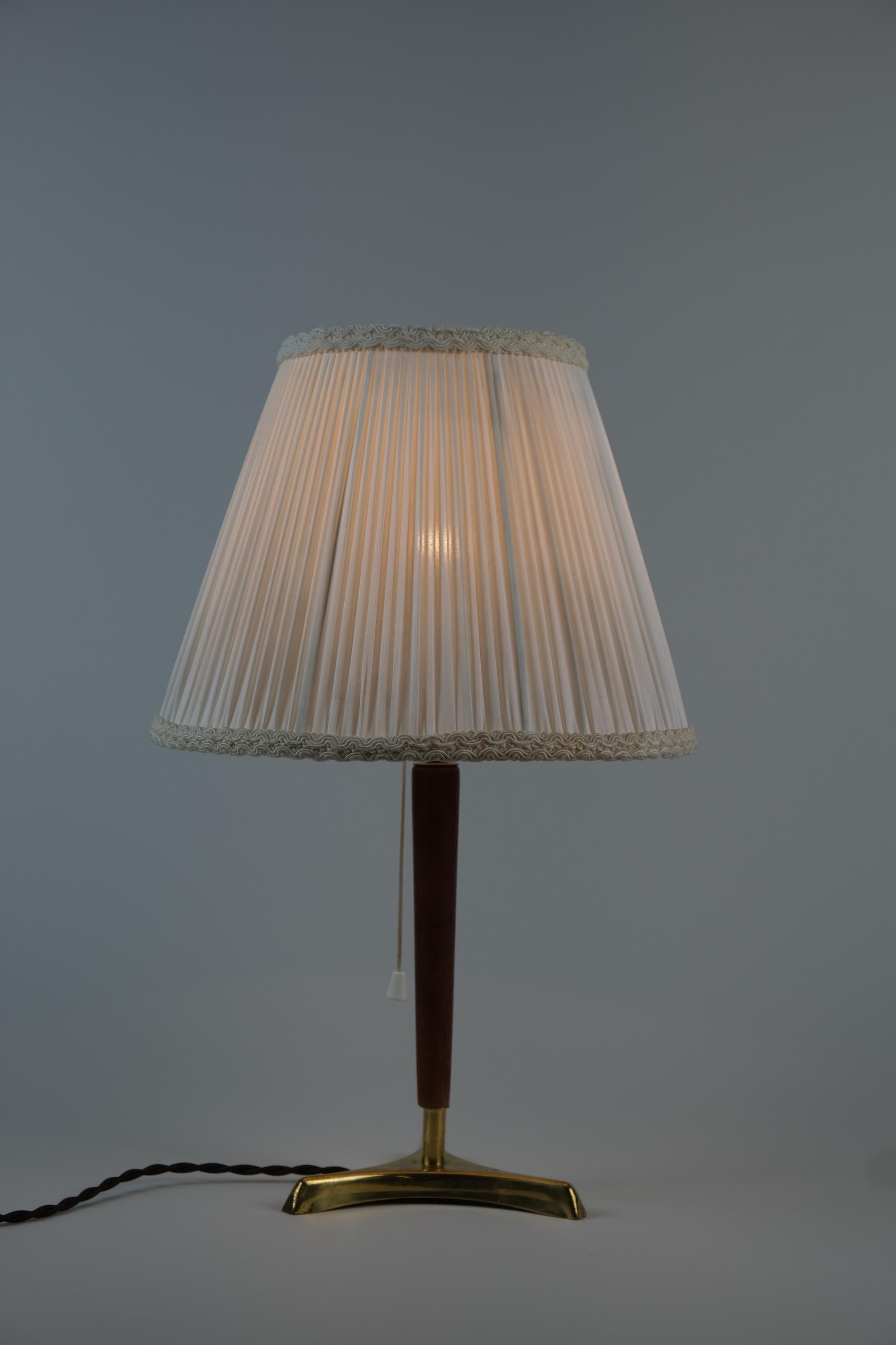 Una preciosa lámpara auxiliar / de mesa modelo 24116 de Valinte Finlandia de los años 60-70. La lámpara tiene una base trípode de latón fundido con un asa de teca y una pantalla de tela sedosa que crea un ambiente acogedor. El soporte de la pantalla