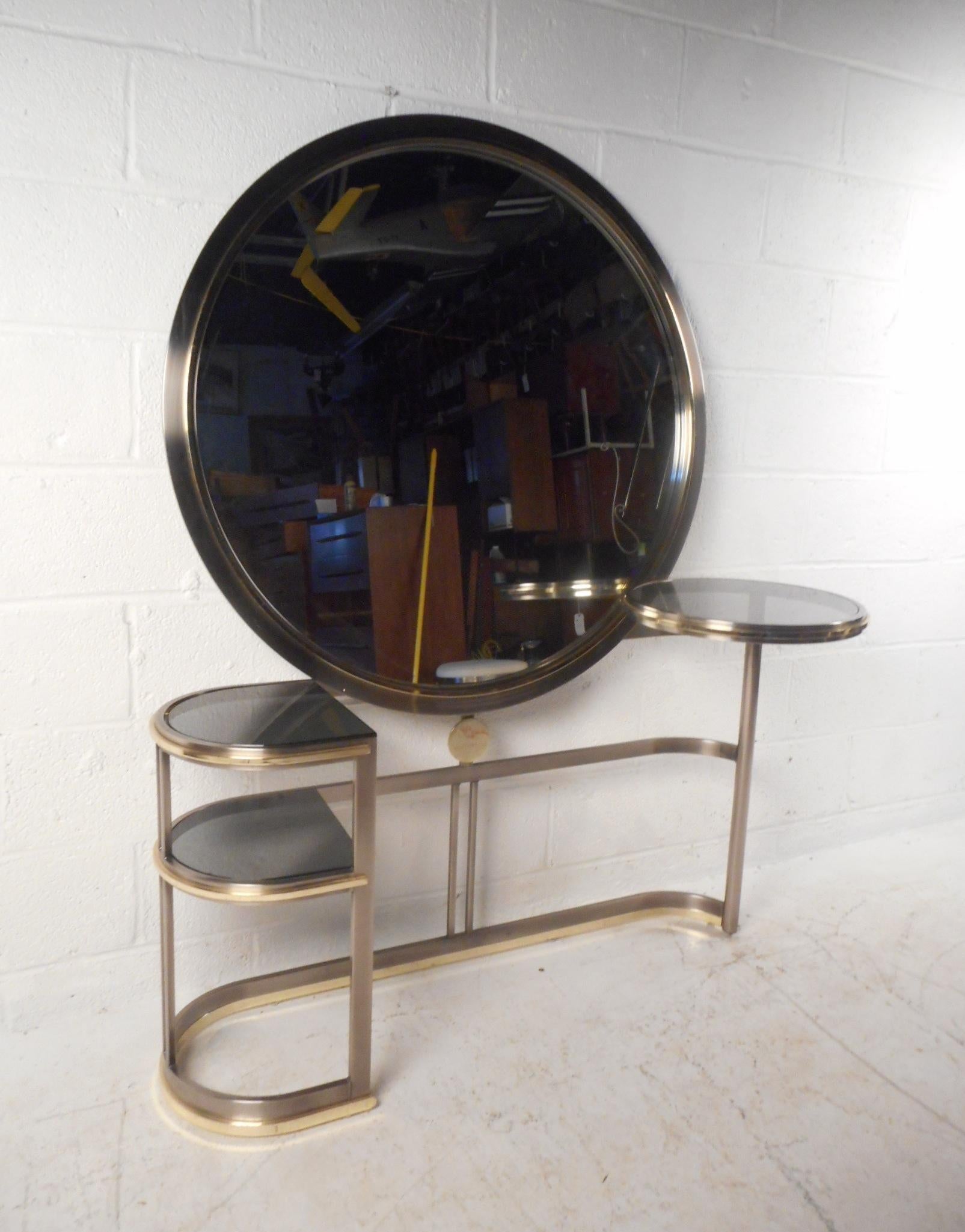 This stunning vintage modern vanity features a round swivel side table on one side with a smoked glass top. The sleek bent metal frame holds a large round mirror in the center with convenient two-tier shelving on one side. This unusual console has