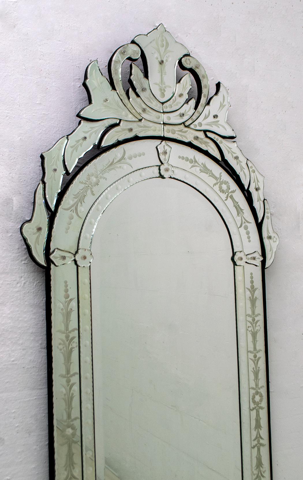 This elegant Mid-Century modern Venetian mirror was made in Italy, circa 1950. It features a cartouche shape with an arched panel and ground mirror in the center. There is a beveled chain around the edges and foliate details throughout. The top of