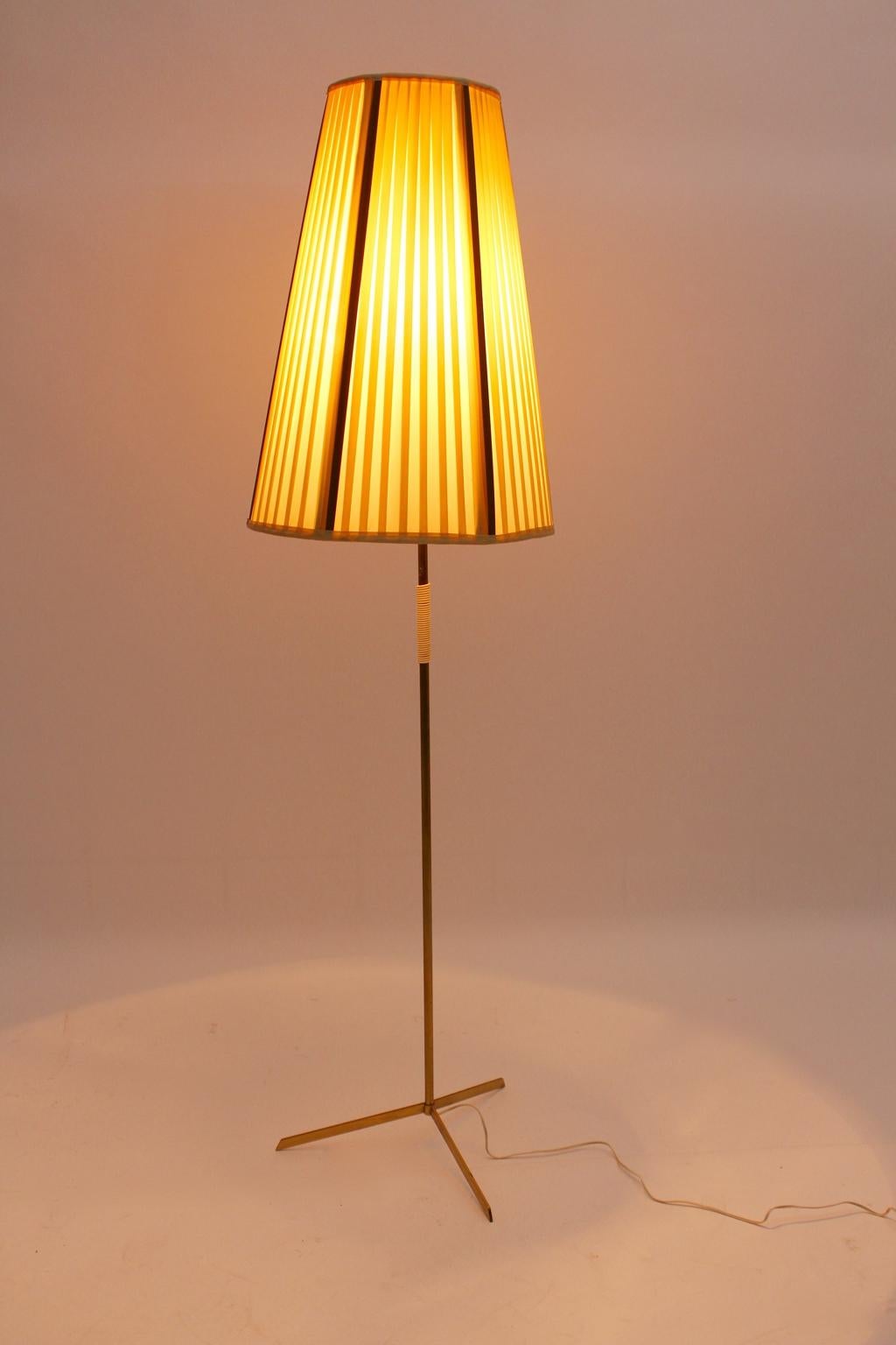 Mid century modern vintage tripod brass floor lamp, which was was designed and made in Vienna, circa 1950.
Also the floor lamp shows an off-white plastic handle grip. The original pleated lamp shade was made of nylon in the base color off white and