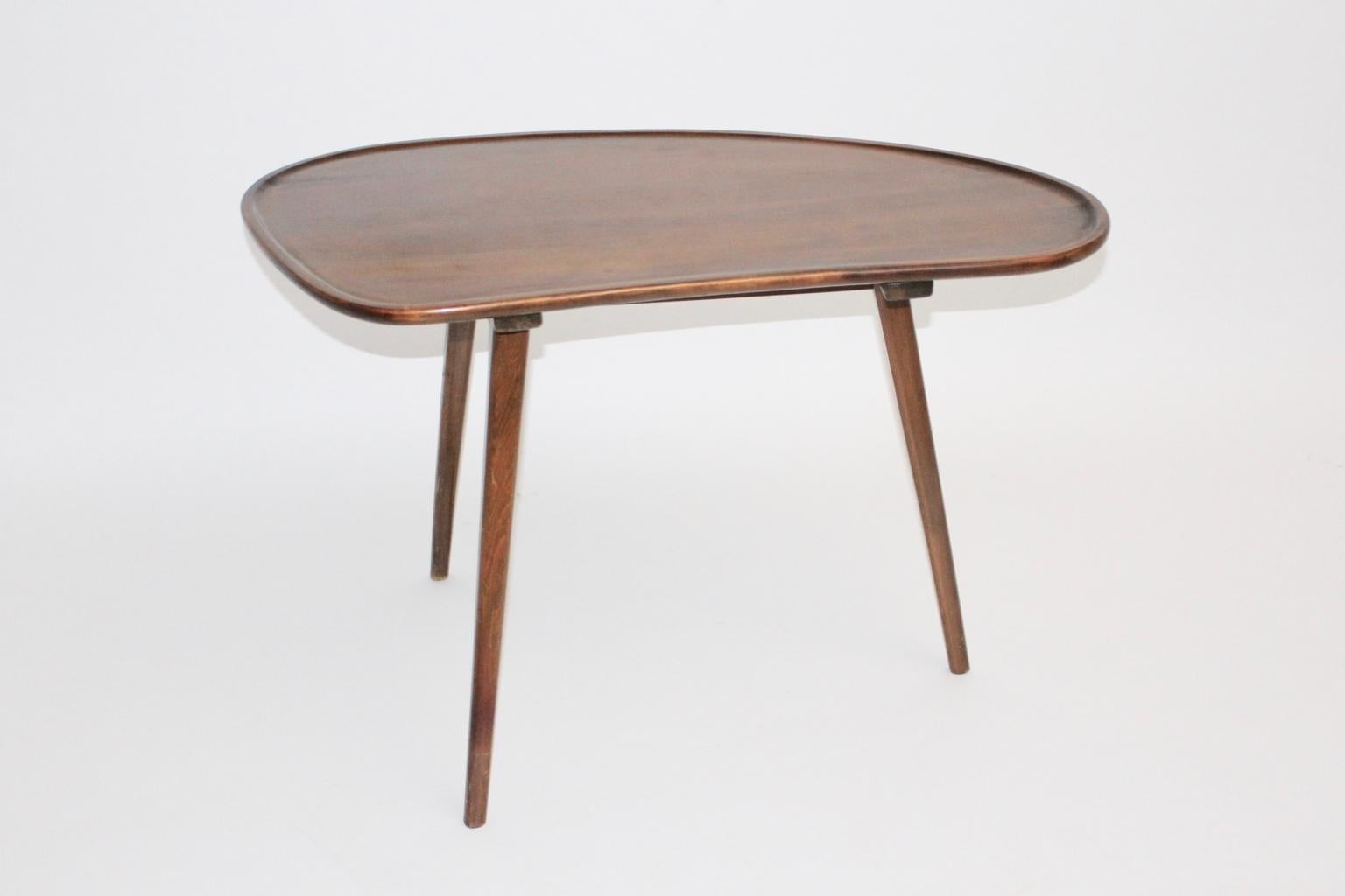 The Mid-Century Modern vintage three legged coffee table was made of beechwood and the tabletop was veneered with cherrywood. The coffee table features a kidney-shape.
The surface is lacquered and the vintage condition is very good and ready to