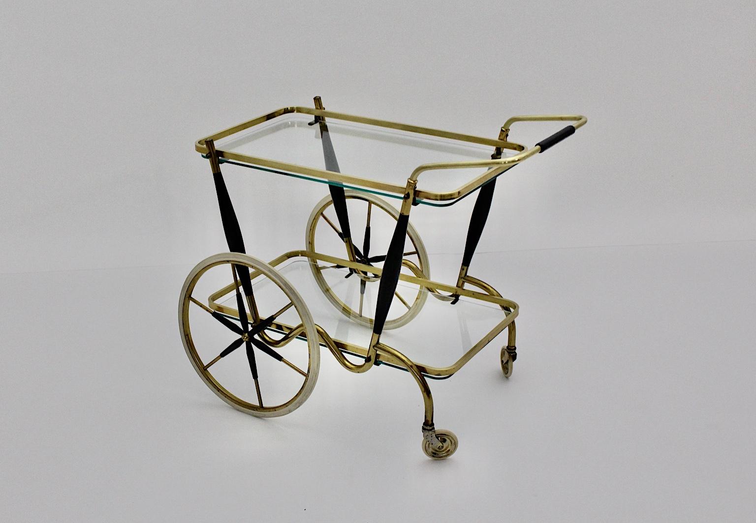 An elegant Mid-Century Modern two-tiered vintage brass cart, which was made out of brass and black lacquered beech.
The bar cart features two small white rubber framed wheels and also two high spoke white rubber wheels, while two clear glass plates