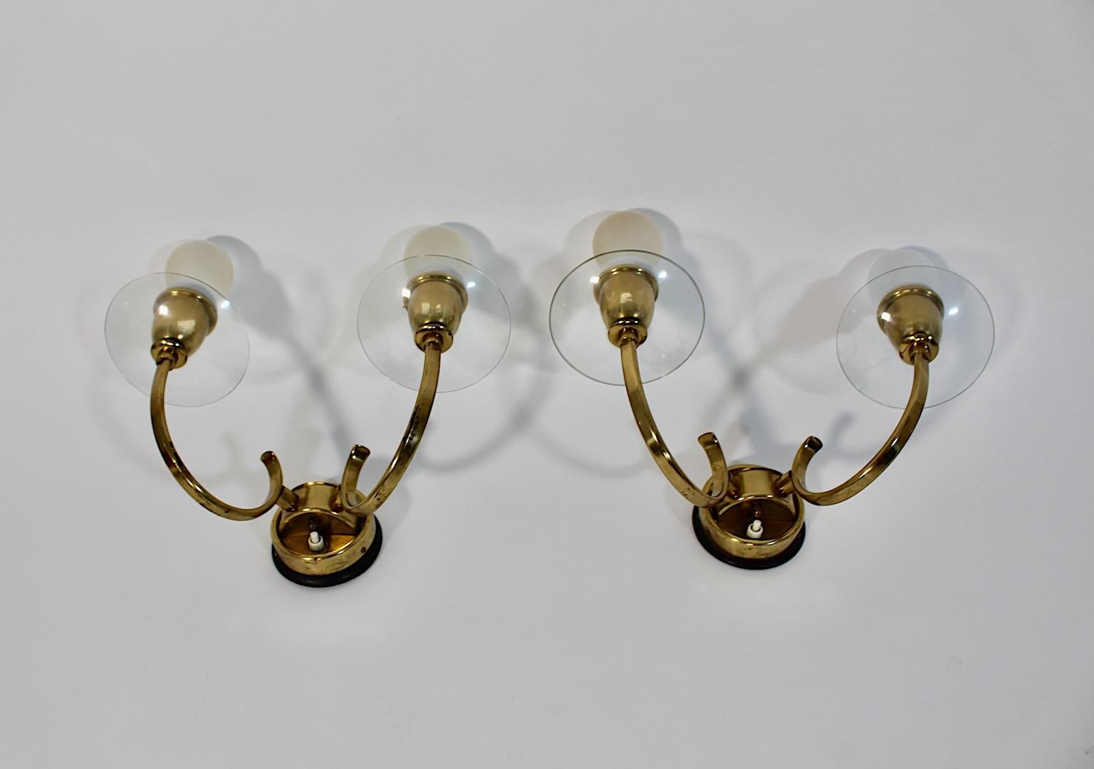 Mid Century Modern vintage pair duo sconces or wall lights from brass and glass 1950s Austria.
An amazing and elegant pair of sconces shows two arms with sockets E 27 
each with slightly curved and graceful glass plates and on/off button at the