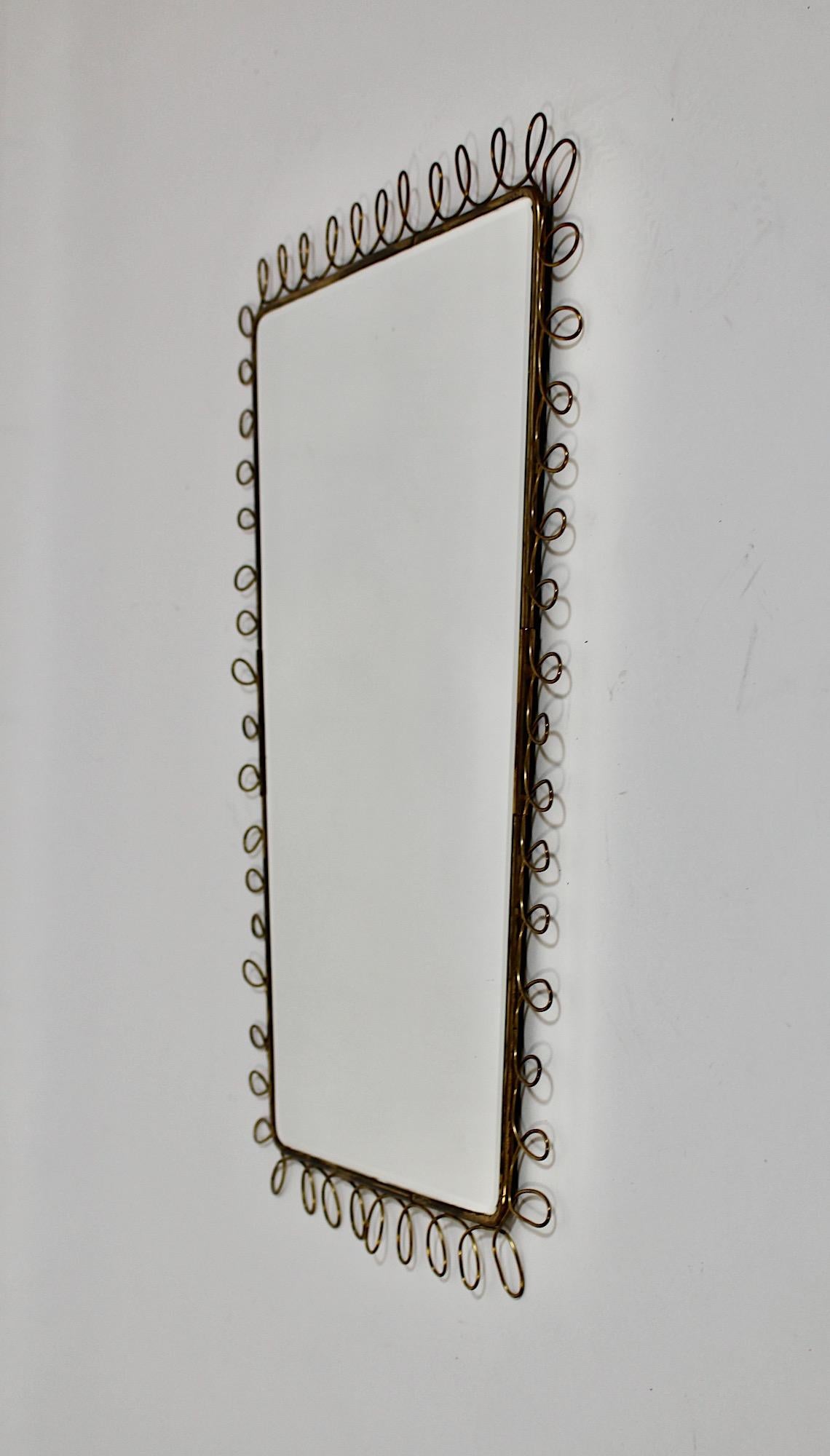 Specchio da parete rettangolare d'epoca Mid Century Modern in ottone e vetro specchiato con anse, disegnato ed eseguito da un artista italiano, anni '50.
Un incantevole specchio da parete vintage di forma morbidamente rettangolare con cornice in