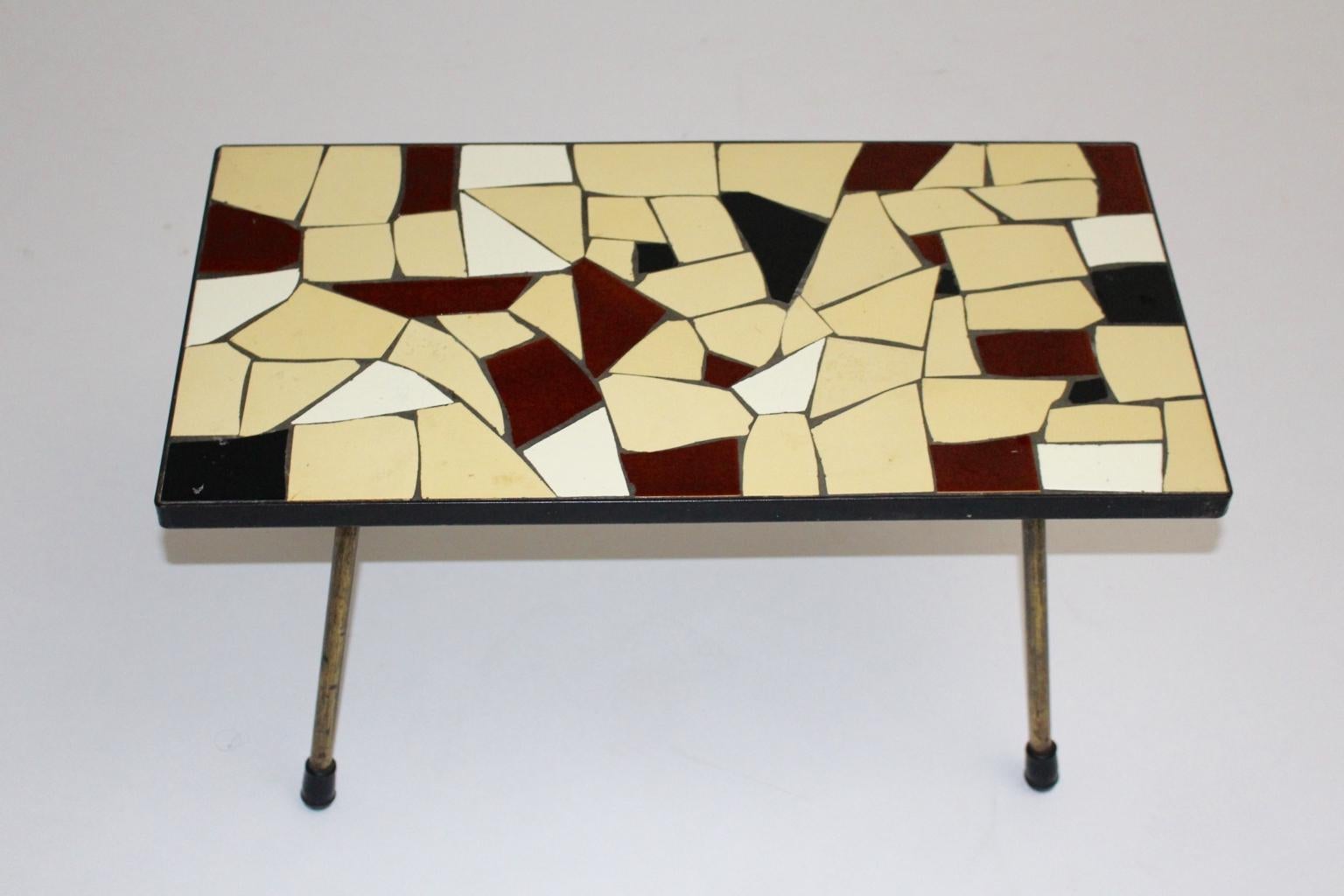 Mid Century Modern vintage sofa table or coffee table, which was designed and executed in Vienna circa 1950.
While the coffee table shows a beautiful plate with ceramic tiles in the colors brown, ivory and white, the brass feet has black rubber