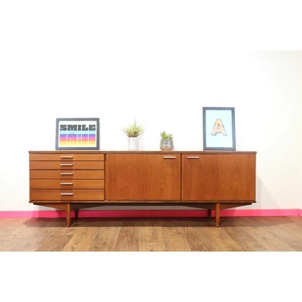 This Mid Century Modern Vintage Danish Style Sideboard Credenza by White and Newton is a stunning piece that is sure to add a touch of elegance to any room. Crafted by the British furniture maker, White and Newton, this credenza exudes the sleek and