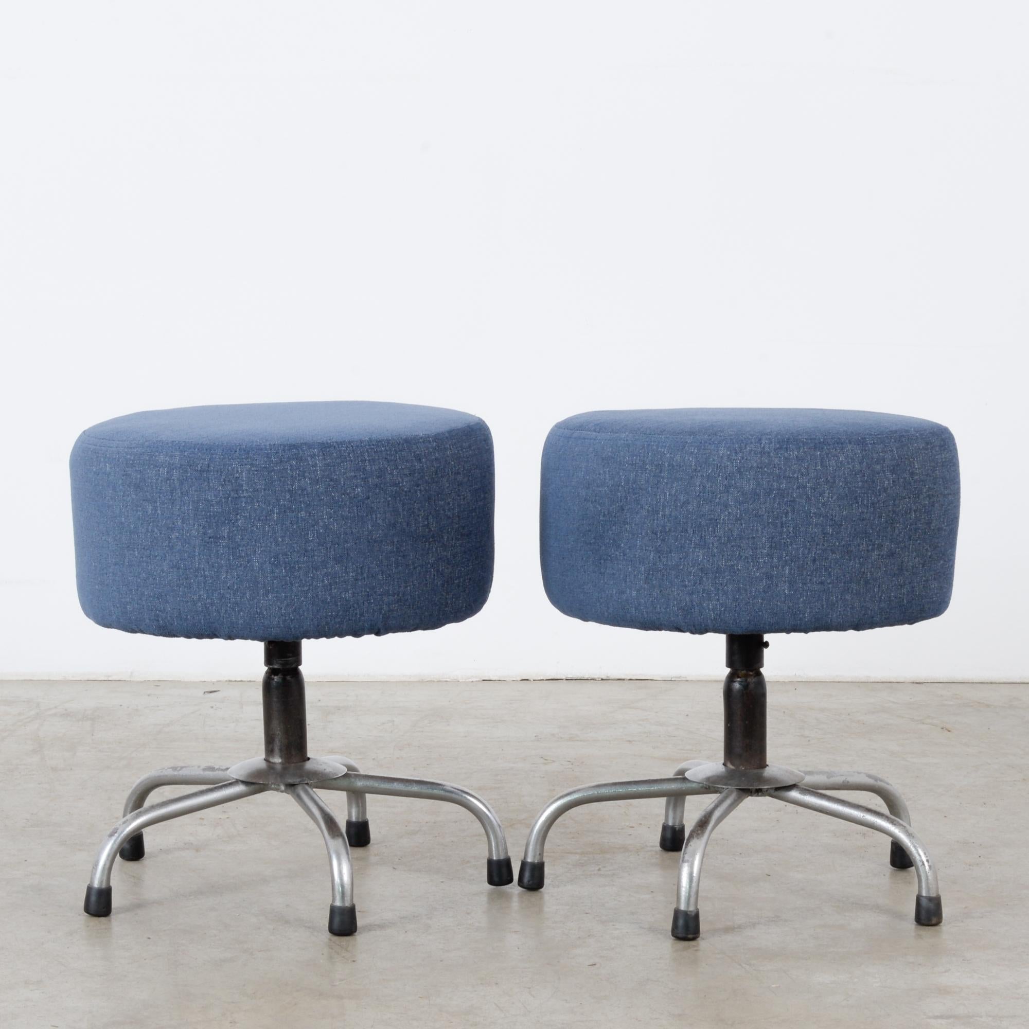 This pair of low metal stools was made in France, circa 1960, and features a comfortable bluish-gray upholstered seat. A central shaft and five curved, tubular legs fitted with black foot caps support the seats.
  