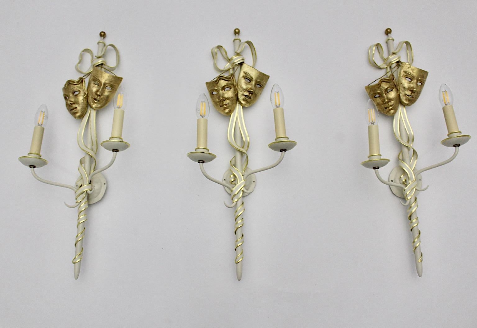  Mid-Century Modern vintage gold and white three ( 3 ) sconces or wall lights from metal with gilded details and solid brass masks, Italy 1940s.
The rare and beautiful hand made sconces were designed in Italy 1940s.
The sconces or wall lights made