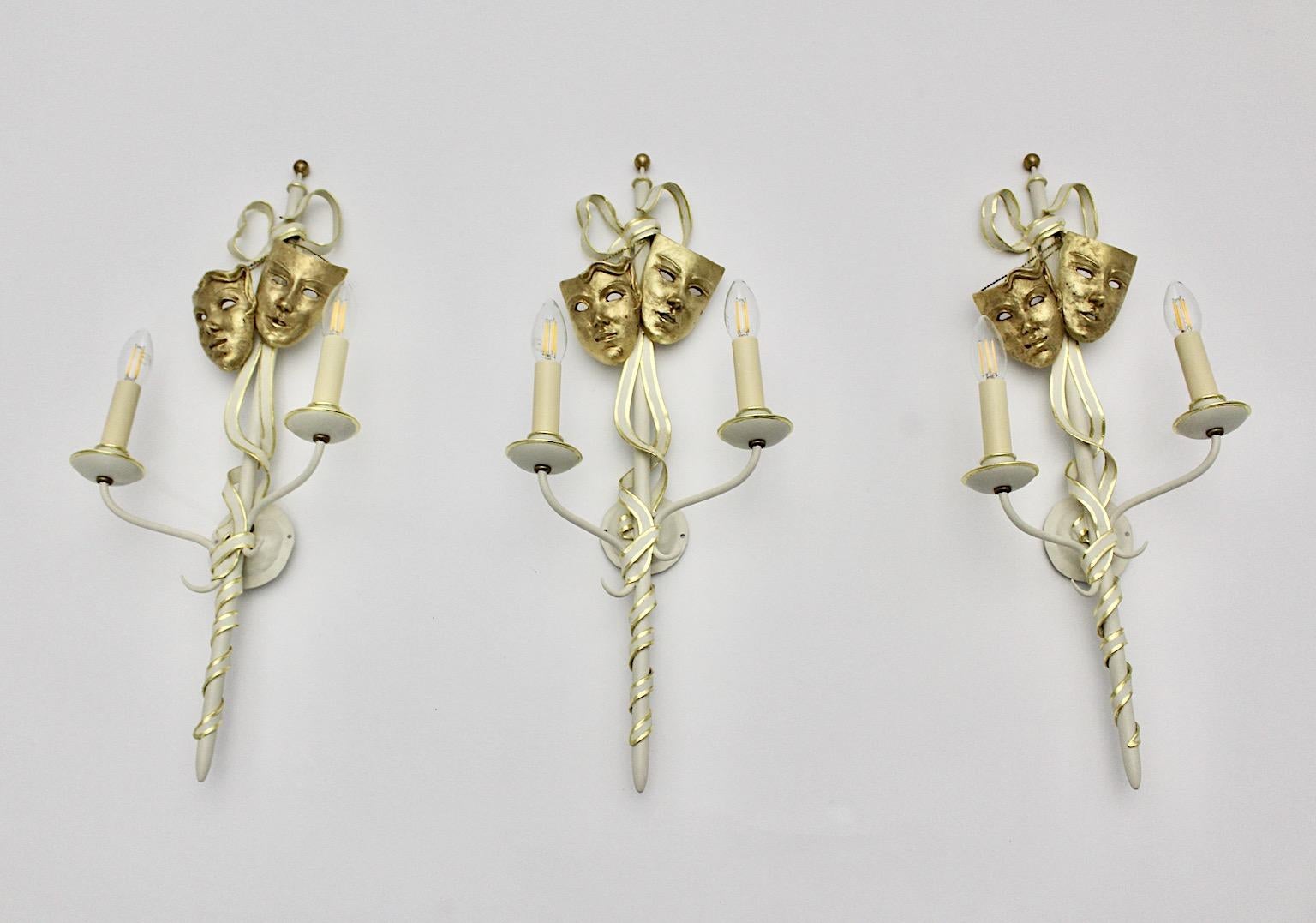 A Mid-Century Modern vintage gold and white set of 3 metal sconces or wall lightings, which shows gilded details and solid brass masks. The rare and outstanding set of sconces was designed and made by hand in Italy, 1940s.
The sconces were made of