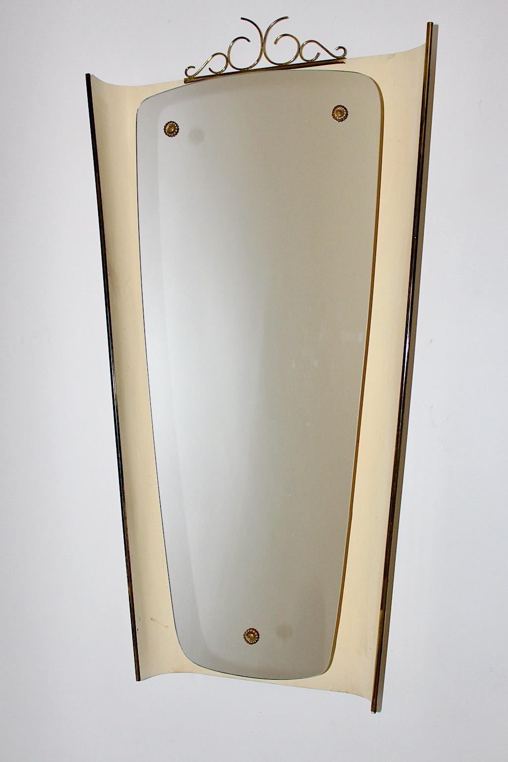 Mid Century Modern Vintage wall mirror with backlit in ivory lacquered metal and brass details 1950s Germany.
While the vintage wall mirror features a slightly curved ivory lacquered metal frame shield like with amazing brass details like loops at