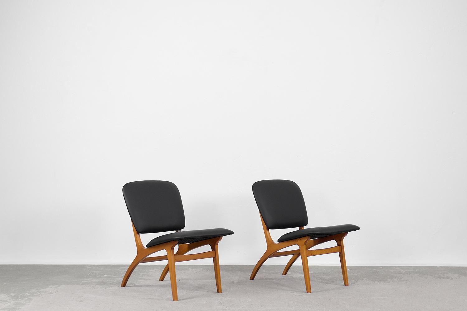 This pair of modernist Jylland armchairs was produced by Jio Möbler in 1953. The frame is made of varnished beech wood. Slender legs gently merge into a subtly tilted backrest. The seat and backrest are upholstered with high-quality black synthetic