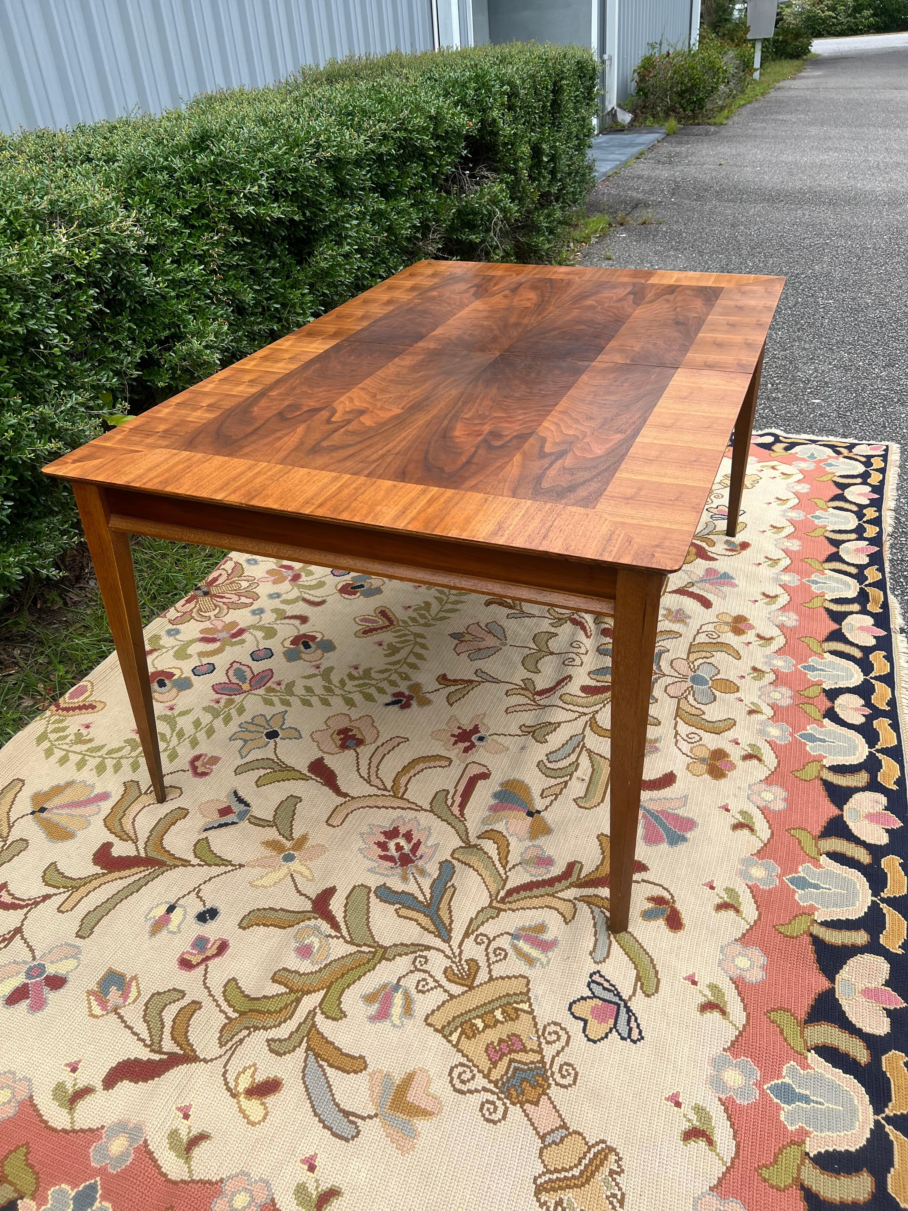 This vintage MCM dining set consists of a table with one 18 inch leaf. This set from the First Edition collection by Lane is in very good original condition with some superficial scratches on the top surface and chipped veneer on the corner of one