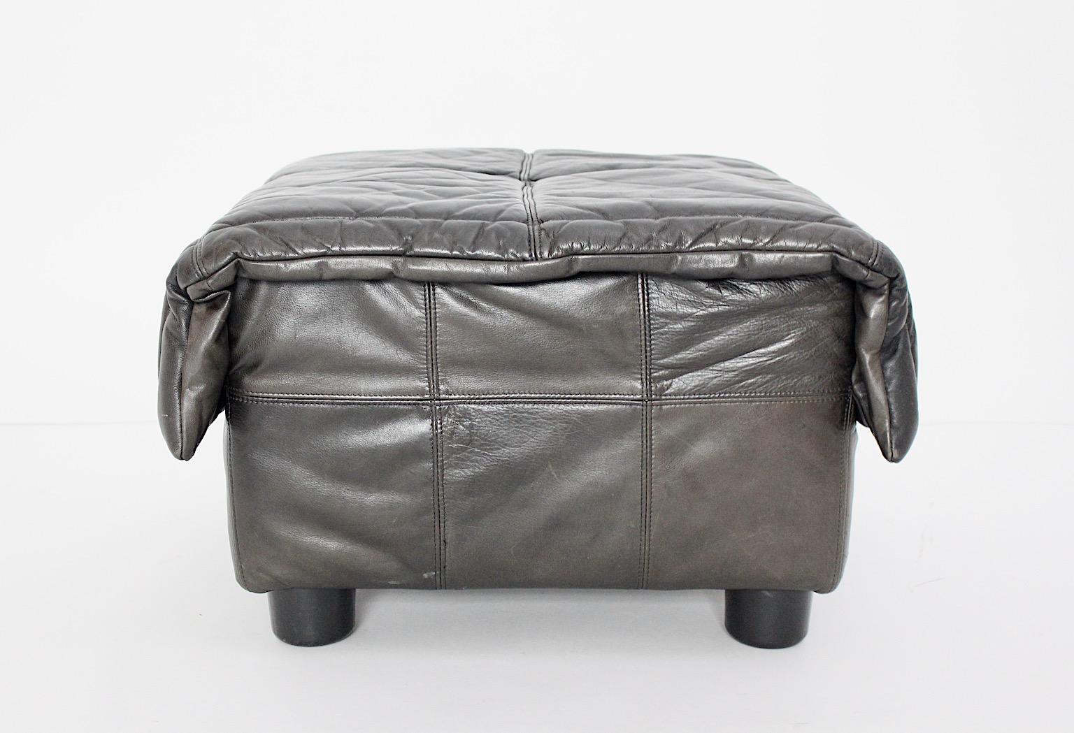 Mid-Century Modern vintage ottoman or stool De Sede style from patinated brown grey black leather with black plastic feet Italy 1970s.
The upholstered leather cloth shows stitched compartments in beautiful patinated leather. The leather color is a