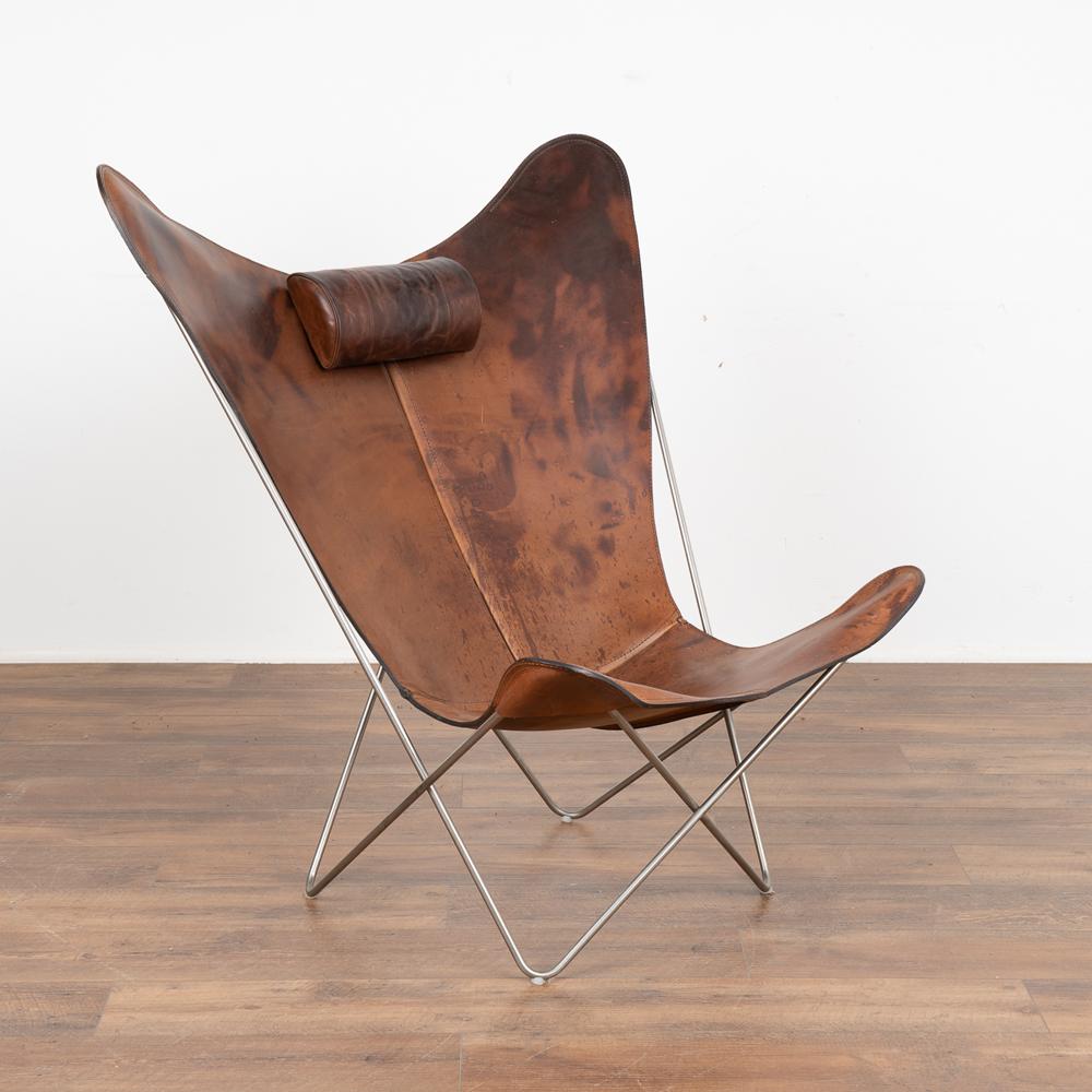 Mid-Century Modern butterfly chair by OX Denmark. KS Chair with steel frame, stretched with cognac-colored leather, loose neck pillow.
Note dark patina of vintage leather; age related stains, scuffs, scratches and wear are commensurate with age and