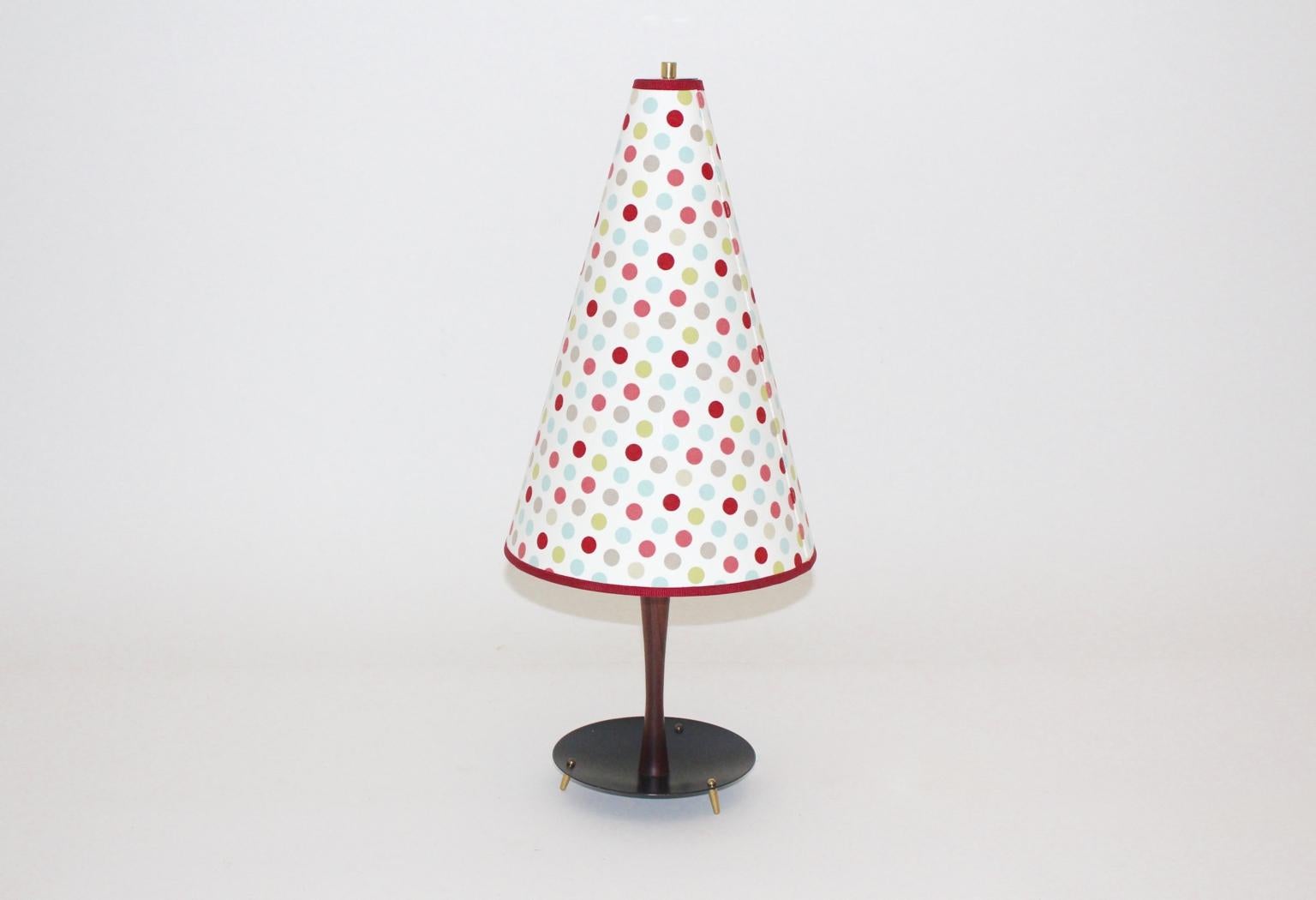 The table lamp shows a mahogany stem with a black lacquered metal base and brass feet.
Furthermore the table lamp features two bulbs E 27 and an on/off switch.
Renewed spotted lamp shade in the colors red, pink grey and green
The vintage