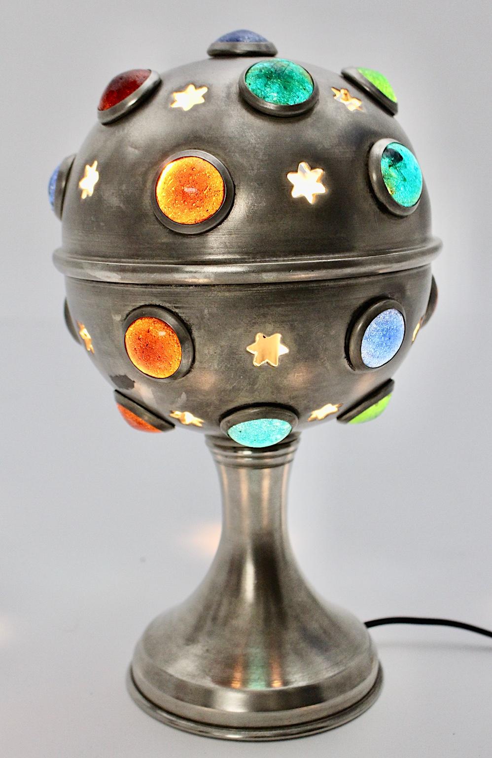 This great Mid-Century Modern vintage Sputnik table lamp was made of nickel-plated brass with 21 multicolored glass eyes (blue, green, light green and orange) and perforated stars.
The blaze through the multicolored glass eyes and the perforated