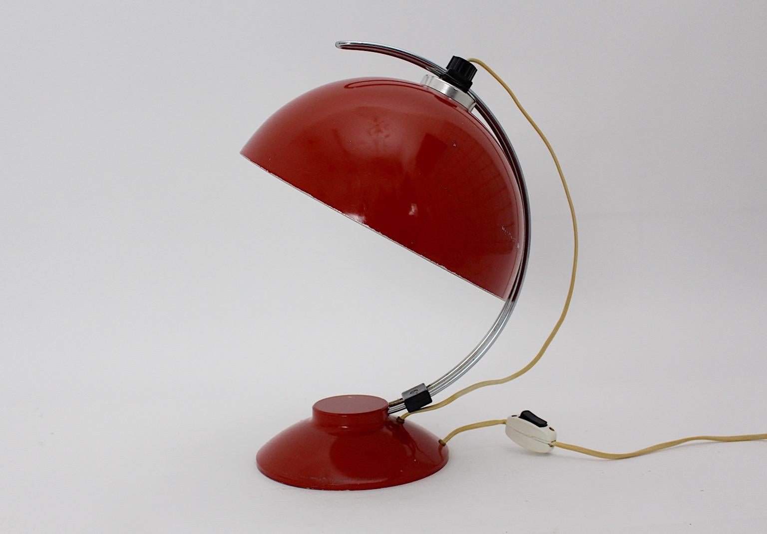 Mid Century Modern vintage table lamp or desk lamp from metal and aluminum in dark red color tone Germany 1950s.
While the base round like is connected through a curved aluminum stem or rail to adjust the lamp shade and fix it with a black plastic