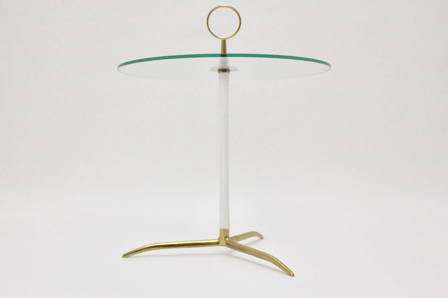 A charming Mid-Century Modern tripod round side table or coffee table with a brass base, which fits in a white lacquered metal stem and a round brass handle. The coffee table is topped with a round clear glass plate.
The overall condition is very