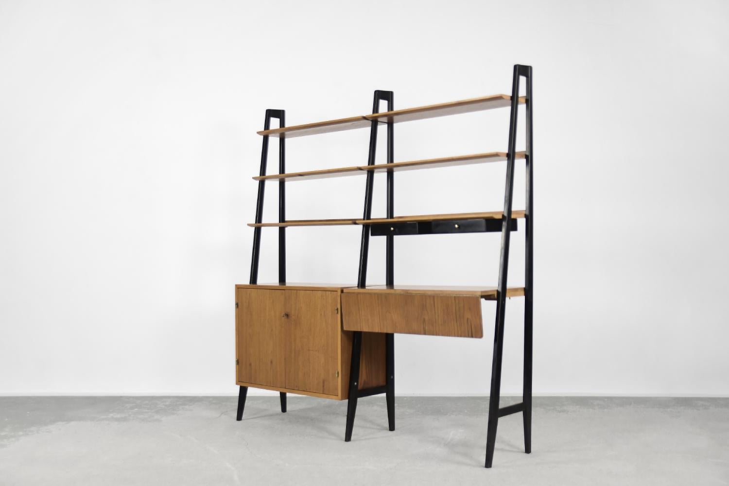 This modular free-standing unit was produced in Scandinavia during the 1960s. It is made of teak wood in a warm shade of brown. It is mounted on high, black legs. This unit has a lockable cabinet with shelves, two small black drawers, 6 shelves and