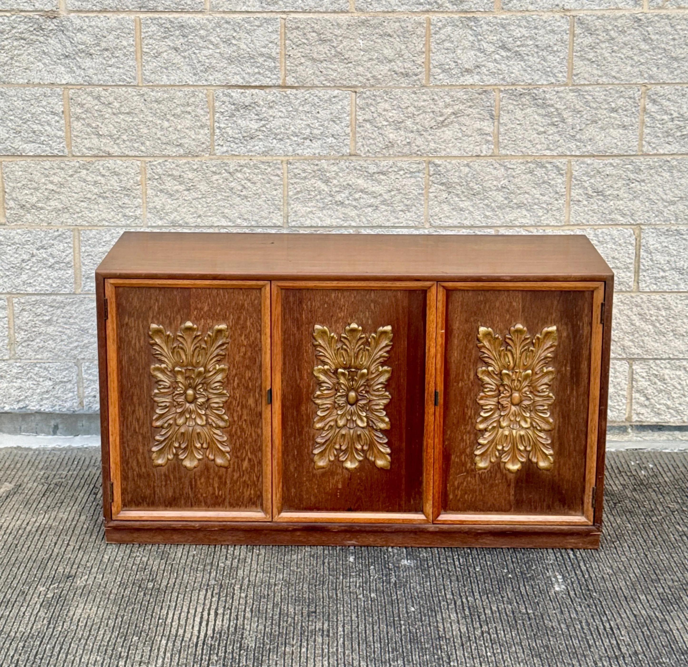 Mobile server a 3 ante in stile Mid-Century Modern con pannelli frontali decorati con motivi floreali in rilievo in tonalità oro. Realizzato in legno dai toni caldi con una silhouette pulita e rettangolare tipica dell'epoca. Ideale come pezzo forte