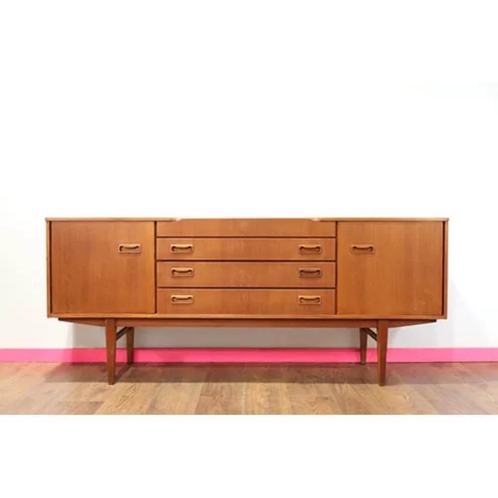 This mid century modern vintage sideboard credenza by Beautility is a stunning piece crafted from teak wood, showcasing the timeless elegance of mid century design. With its sleek silhouette and minimalistic hardware, it seamlessly blends form and