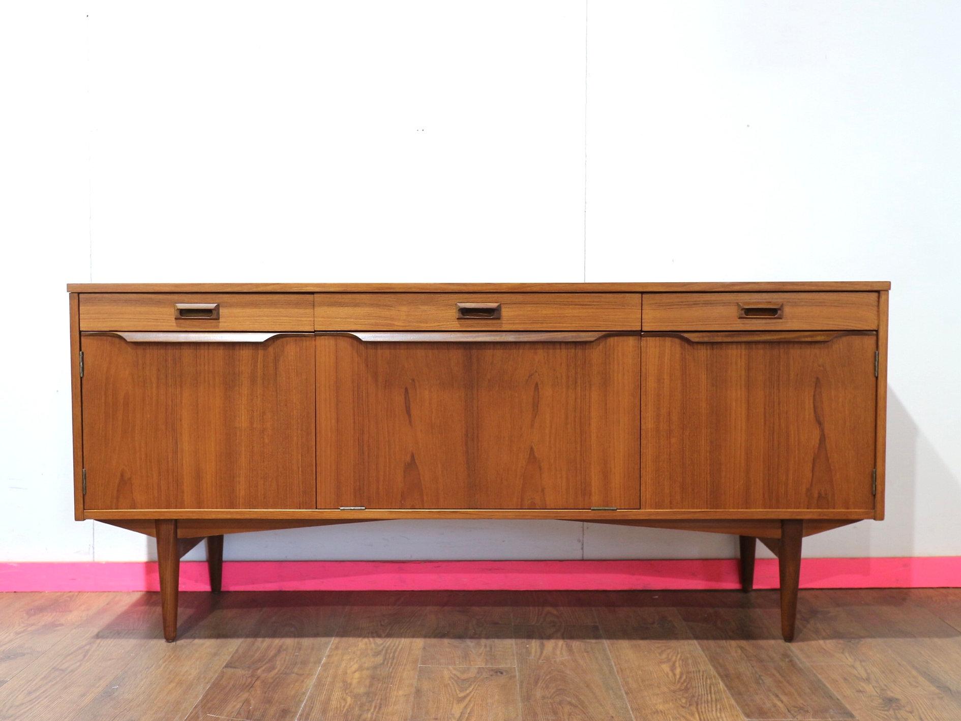 Eleva il tuo spazio abitativo con la credenza Mid Century Modern Vintage di Elliots of Newbury, progettata in stile danese senza tempo. Questa splendida credenza compatta vanta una bellissima venatura che ne esalta l'estetica, offrendo allo stesso