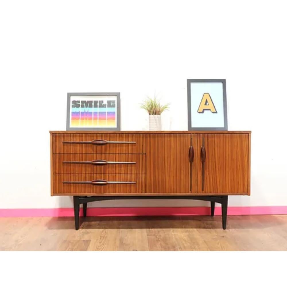 This mid century modern vintage sideboard credenza by Elliots of Newbury is a stunning addition to any home or office. Made by the renowned British furniture maker, this piece is a true testament to the quality and craftsmanship of mid century