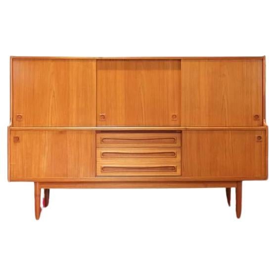 An stunning midcentury sideboard by Danish cabinet maker and designer Johannes Andersen. The upper section with oak and baize lined slide trays to the left, adjustable shelves to left and center. The lower section holding three central drawers with