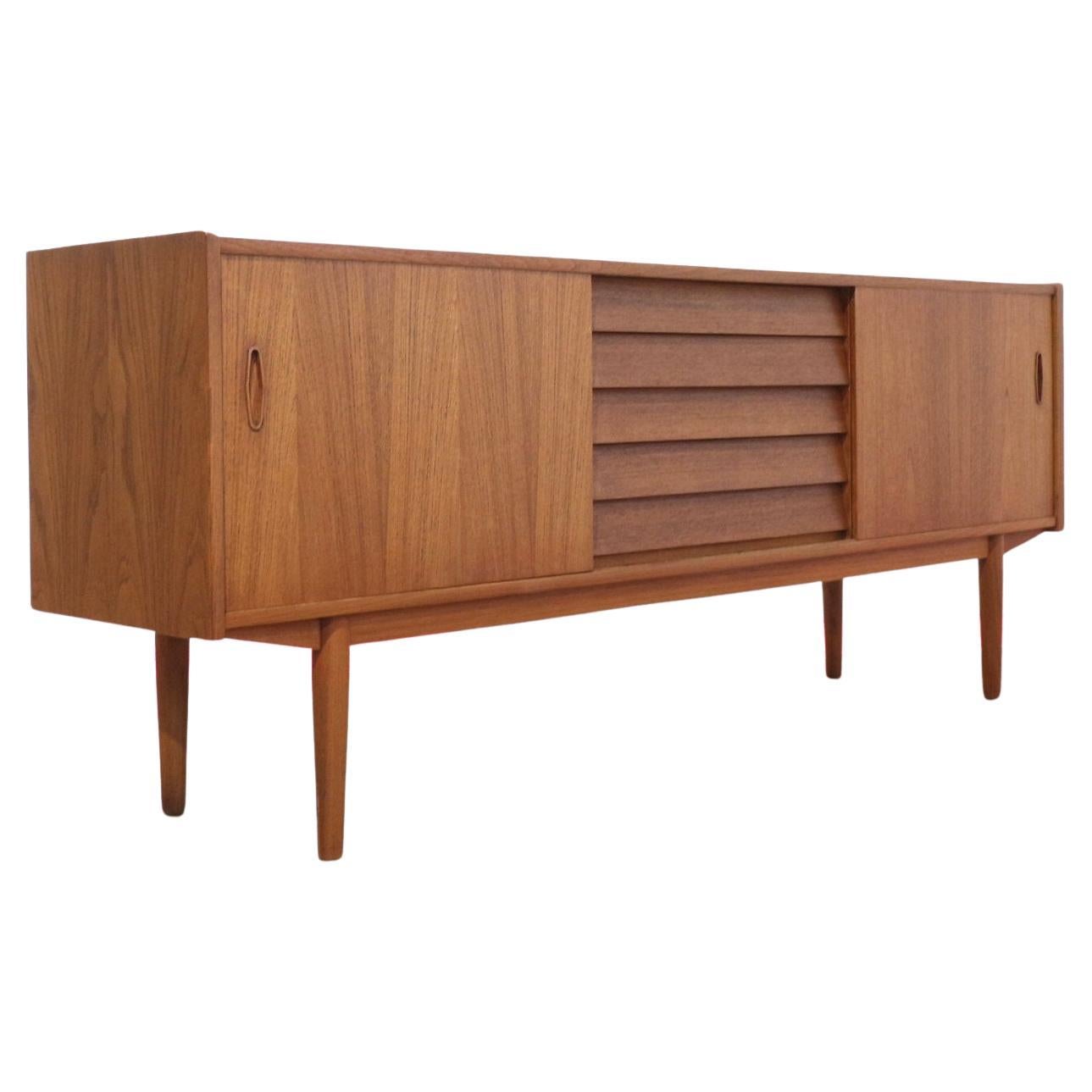 Discover the stunning credenza by renowned Swedish furniture maker Nils Jonsson, a masterpiece embodying true Scandinavian style.This exquisite teak sideboard effortlessly combines elegant design with great storage solutions. Perfect for any