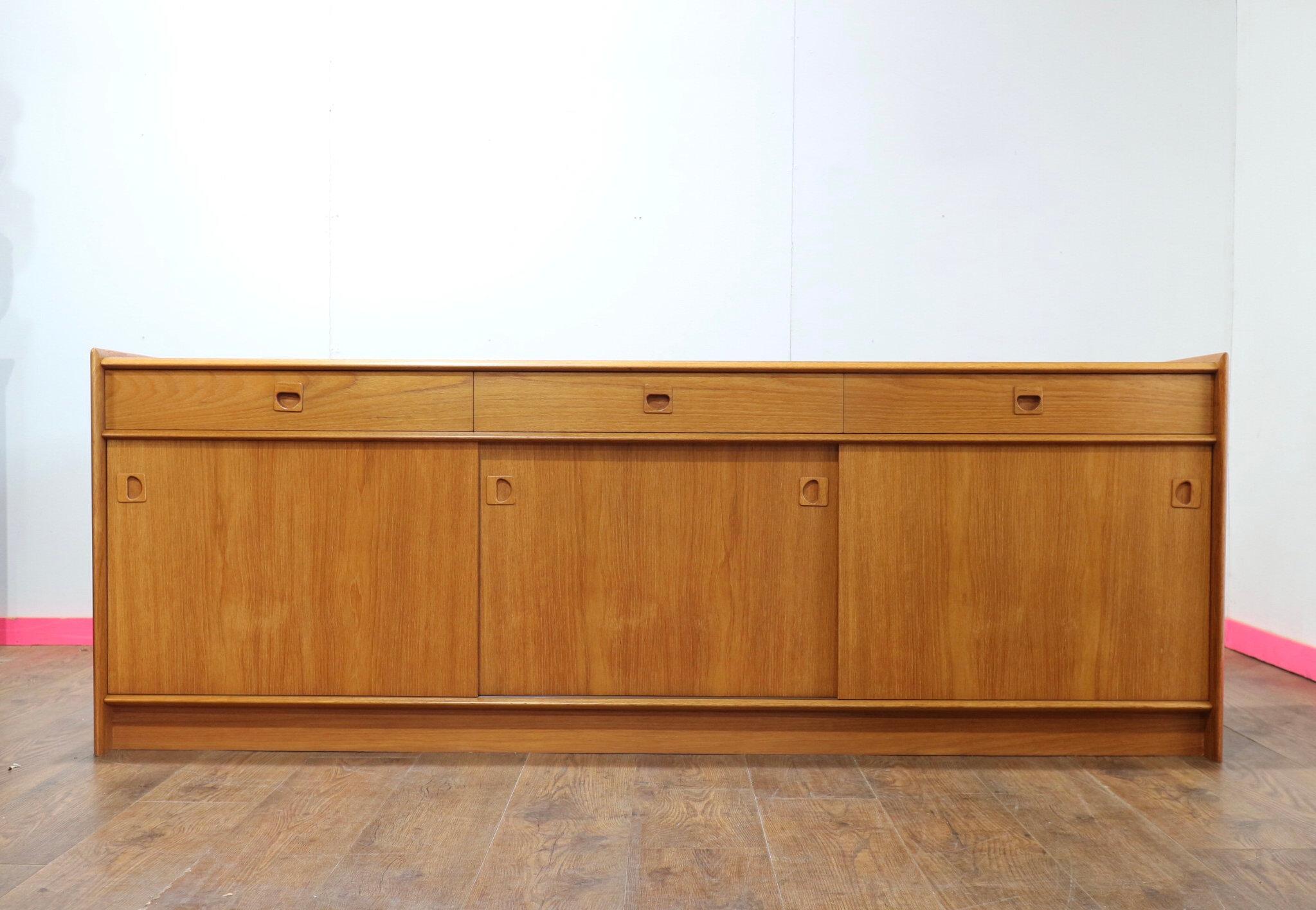 Enhance your living space with this stunning Danish credenza from Mid Century Traders. Expertly crafted from vintage teak, this low Danish sideboard offers exceptional storage with its sleek sliding doors, combining both functionality and style.