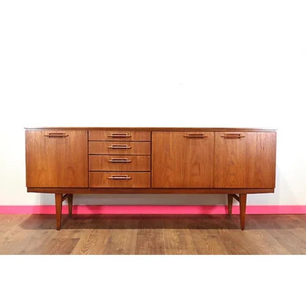Beautifully crafted by British furniture maker Beautility, this mid-century modern teak sideboard credenza is a stunning addition to any home. With its sleek design and sculpted handles, this credenza exudes style and sophistication, setting it