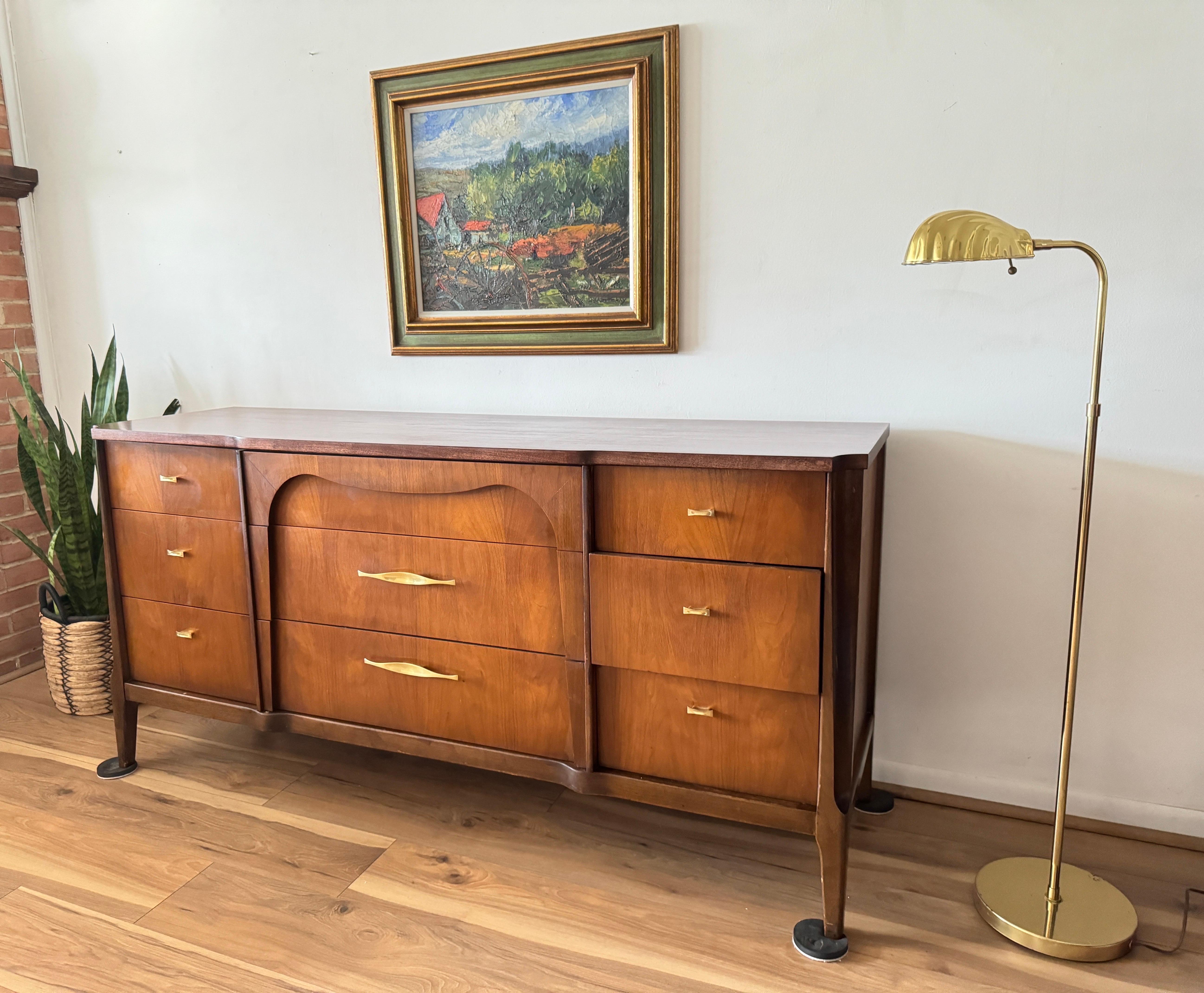 The Mid-Century Modern Broyhill Emphasis Walnut Credenza features nine pull-out drawers adorned with elegant brass handles, accentuated by intricate layered detailing on the central drawers.

