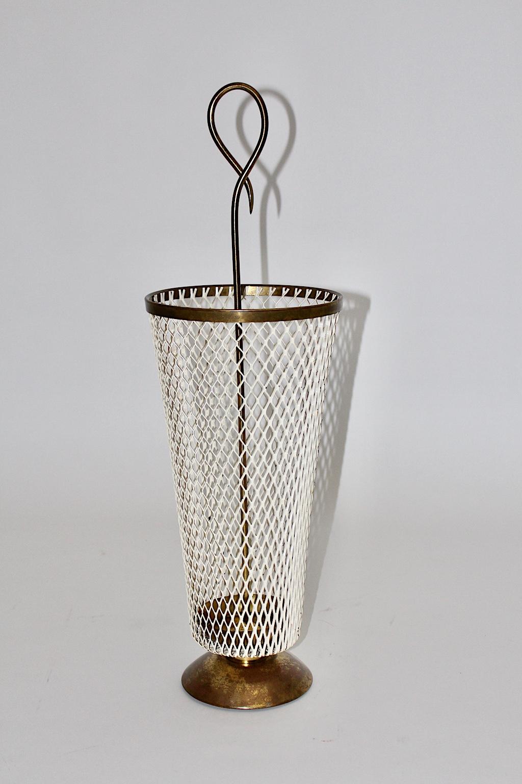 An amazing Mid-Century Modern metal vintage umbrella stand designed by Mathieu Matégot attributed France 1950s, which shows elegant brass details. The basket of the umbrella stand was made out of white perforated metal while the handle, the edge and