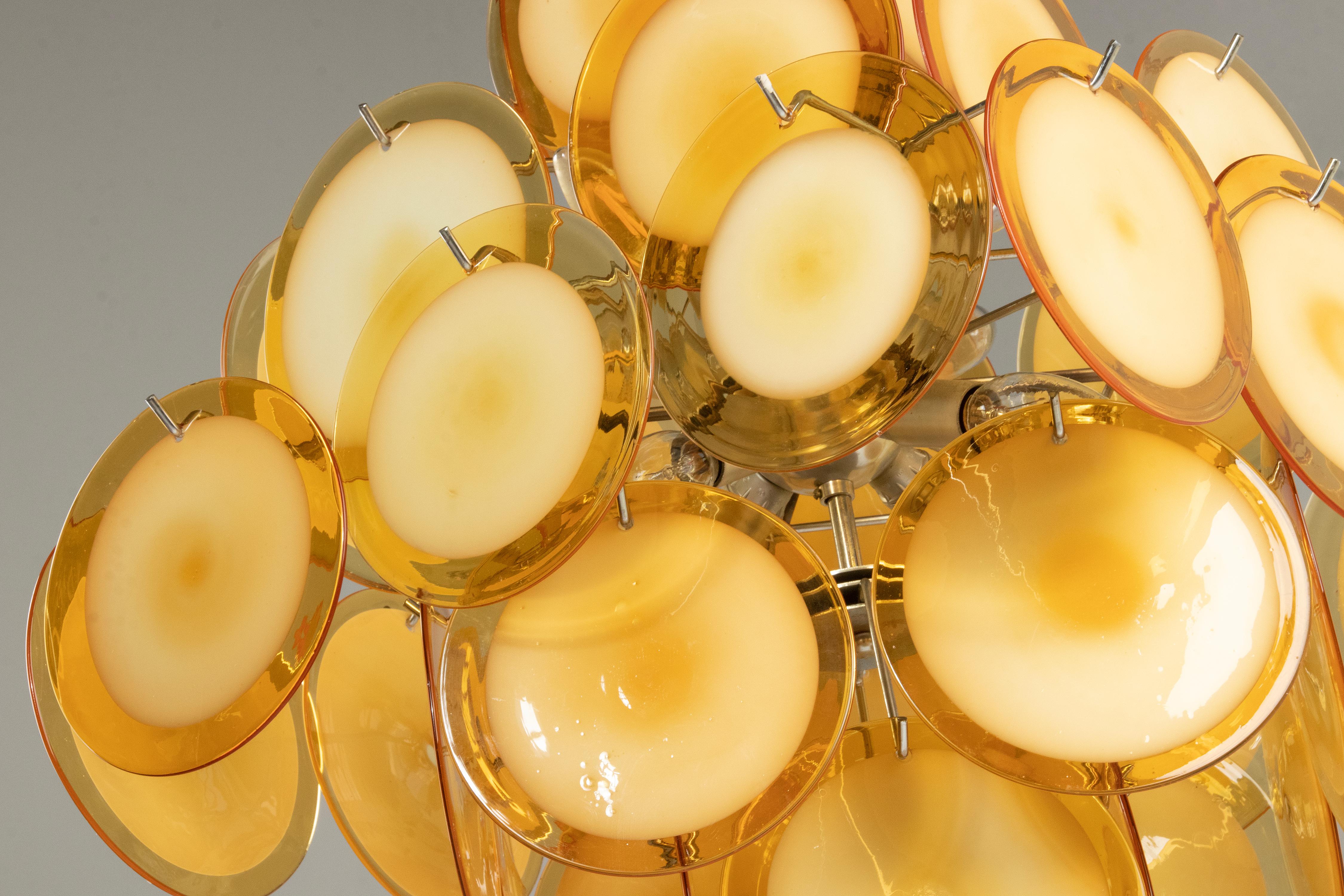 An Italian Murano chandelier attributed to Vistosi. The chandelier has 36 hand blown glass disks made of yellow/orange Murano glass, hanging in a metal frame. The lamp has 8 lights (E14 sockets), which gives an atmospheric light. Made in Italy
