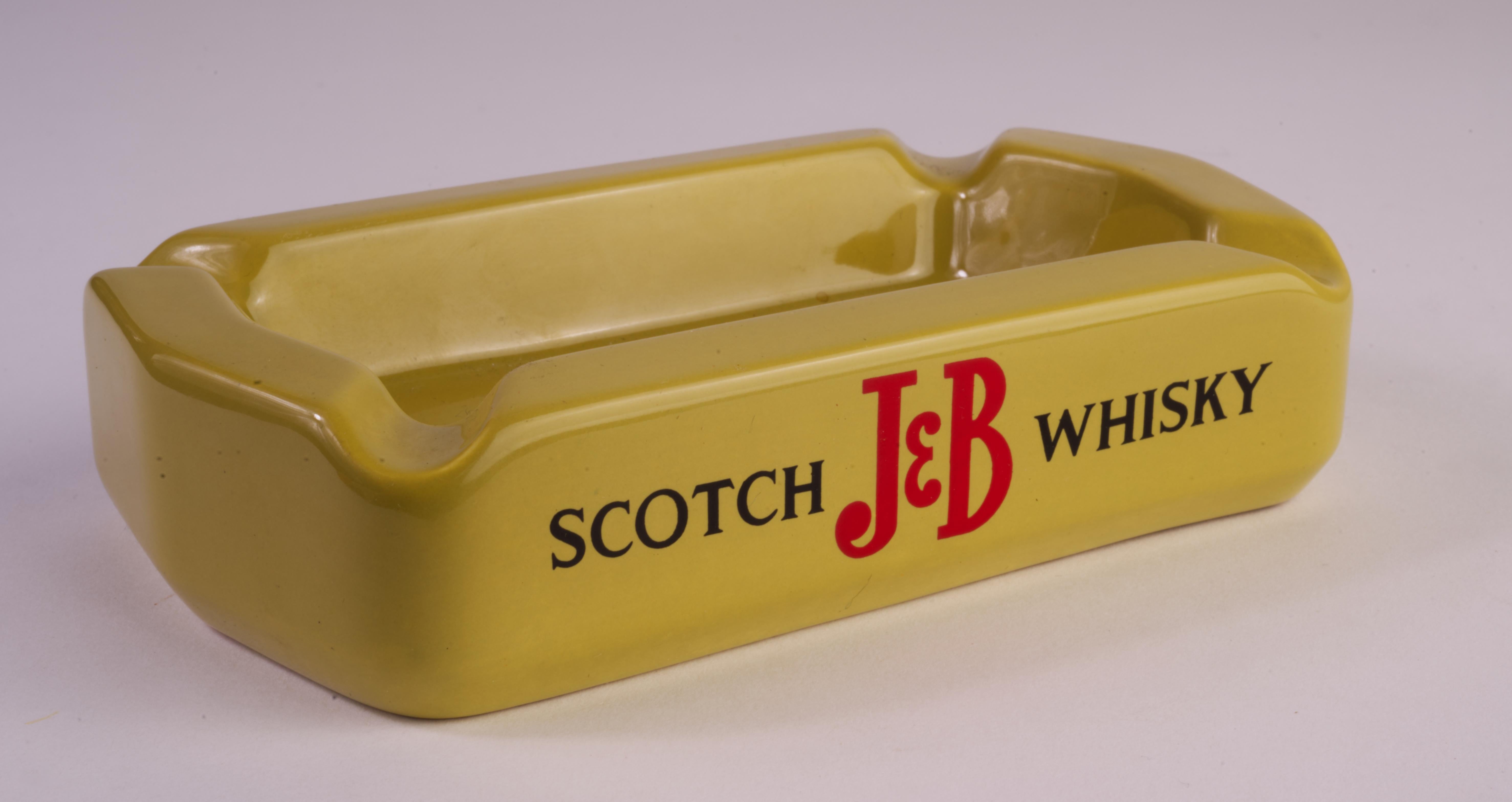  Cendrier publicitaire en céramique vintage Mid Century Modern J&B Scotch Whisky a été fabriqué en Angleterre par Wade Pottery. Le cendrier rectangulaire avec des porte-cigarettes à chaque coin est émaillé d'une glaçure brillante jaune moutarde