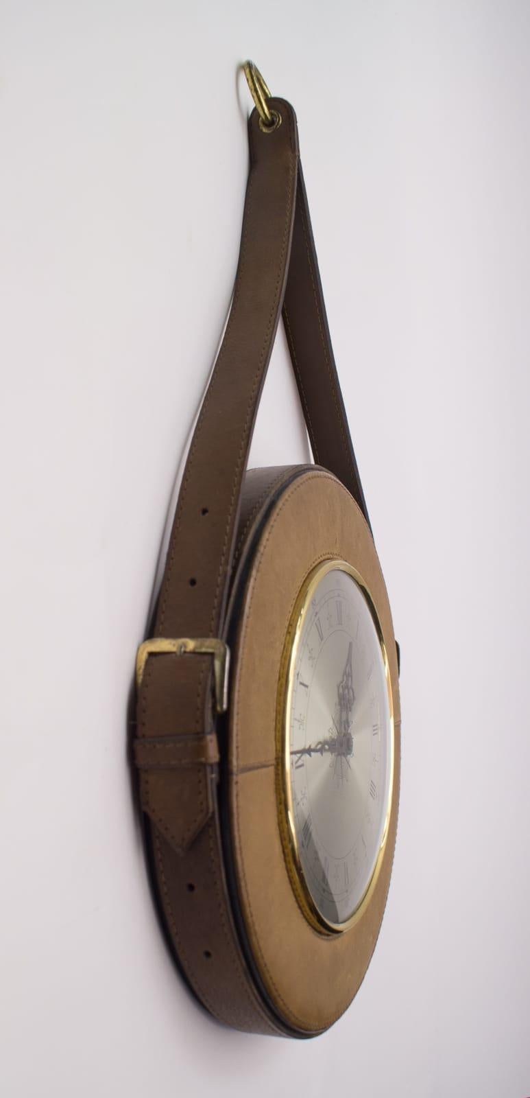 The clock is round, surrounded by leather straps, connected by brass hinges as belt buckles. The Brass ring allows it to be suspended.

Made in Germany.

Electric, battery operated clock.