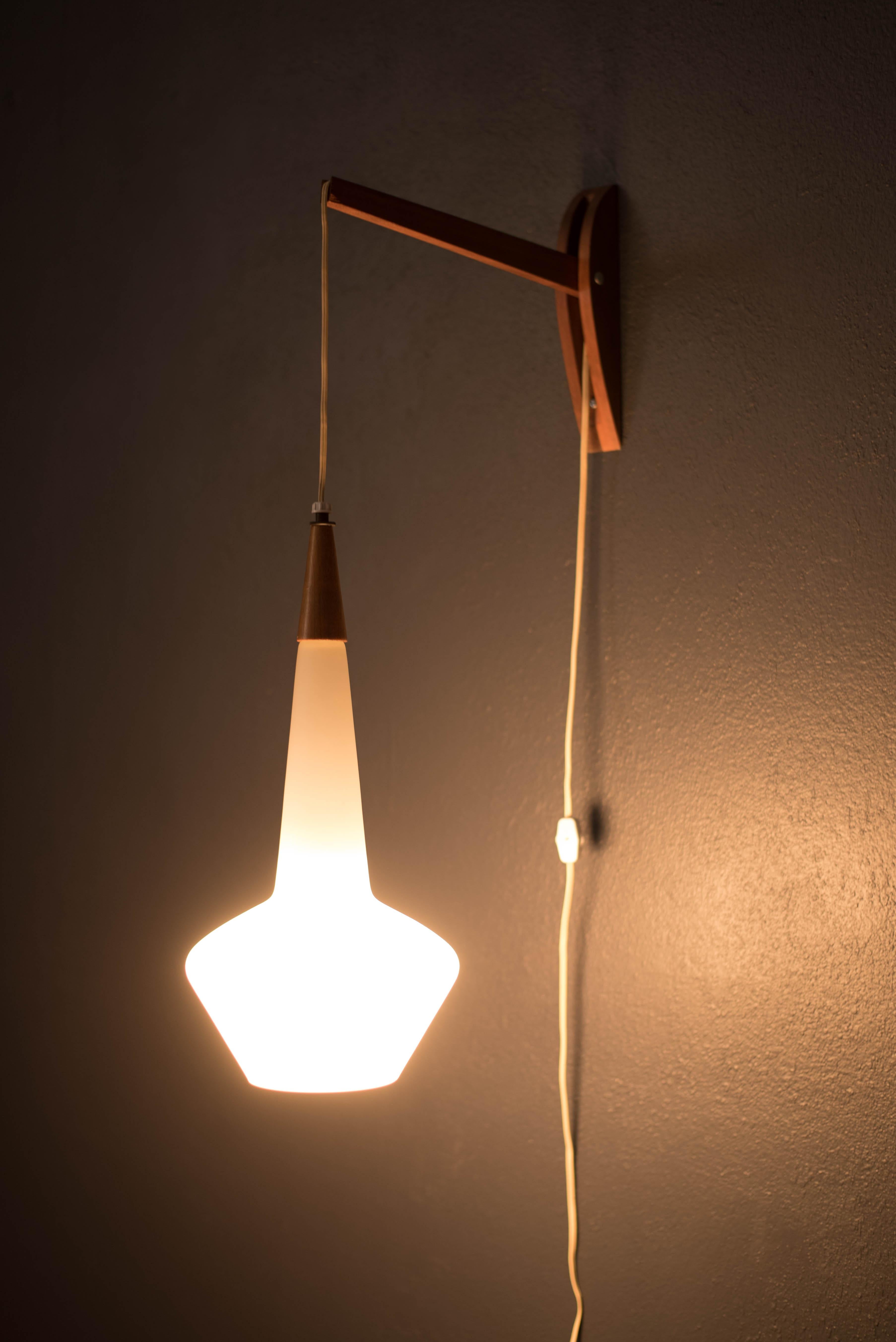 Vintage hanging wall mount light fixture circa 1960's. This piece features a glowing frosted white glass pendant accented with walnut trim. Includes an adjustable cord that allows the pendant to be displayed at different heights. Perfect to use a