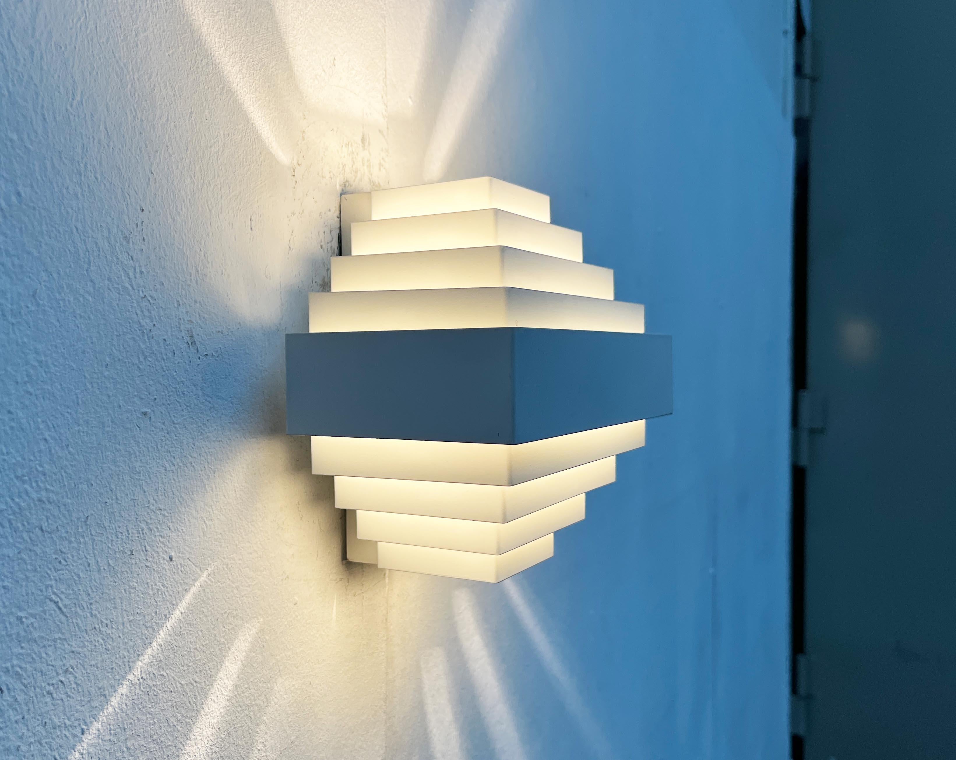 Dos apliques de pared basados en un diseño del arquitecto y diseñador belga Jules Wabbes de los años sesenta.

Un diseño minimalista. El llamativo cuerpo de la lámpara está formado por finas lamas metálicas dispuestas de forma escalonada. Las lamas