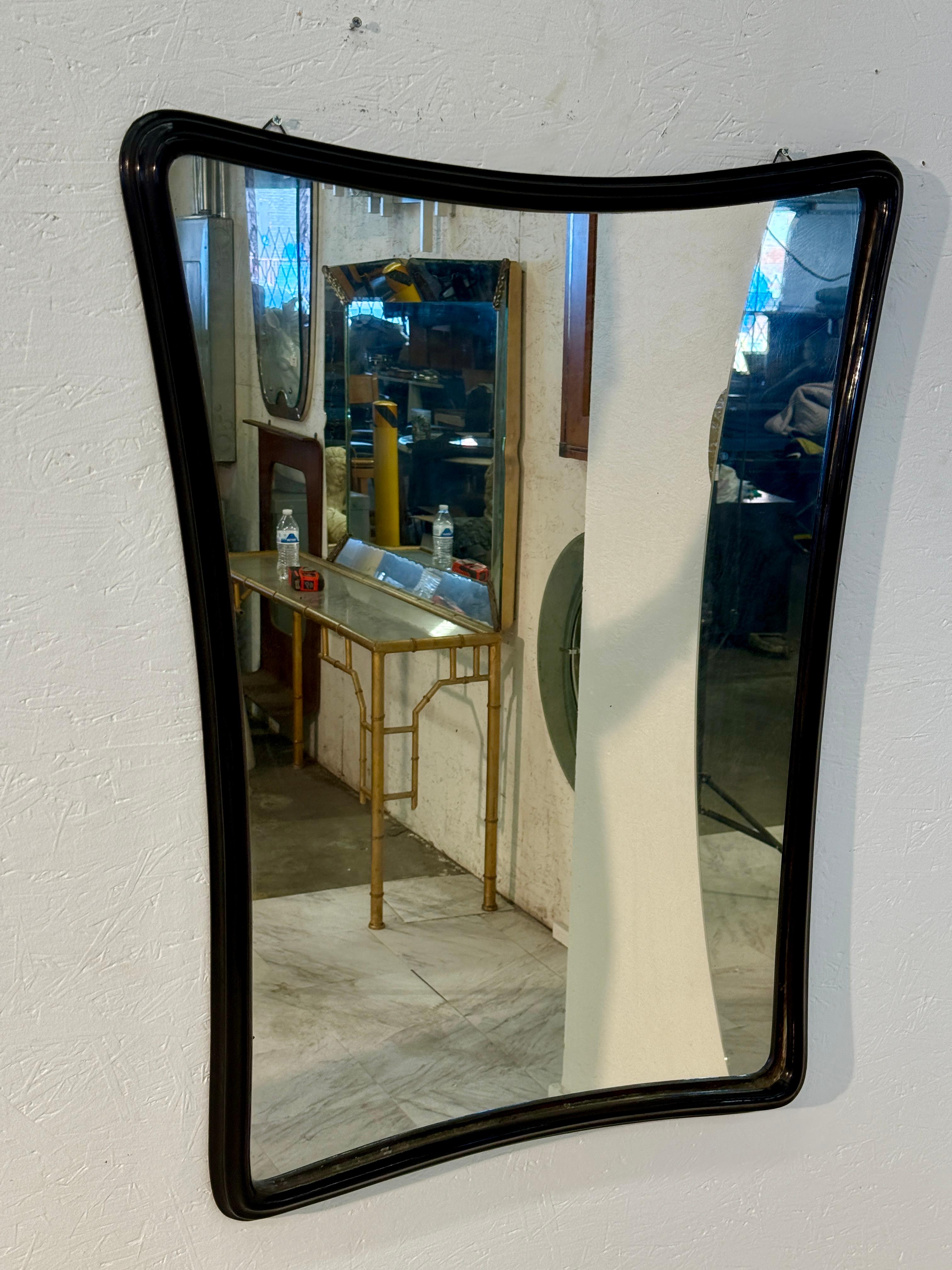 Miroir moderne du milieu du siècle, doté d'un cadre sculptural en bois laqué noir. Sa forme subtilement incurvée et asymétrique ajoute du mouvement et de l'intérêt visuel tout en conservant un aspect épuré et minimaliste. Le verre du miroir est en