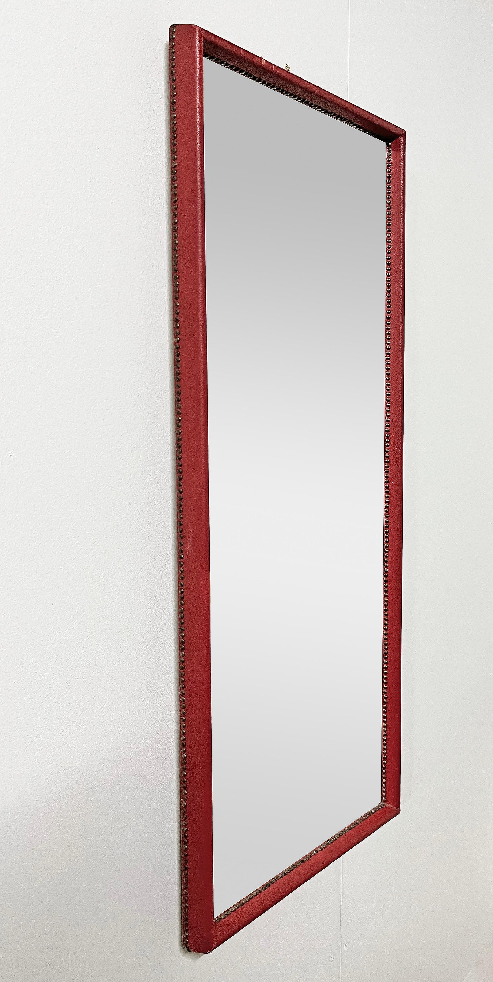 Wall mirror attributed to Otto Schulz, 1940's. Frame dressed in dark red faux leather, decorated around the inner and outer edges with brass nails.
Wear and patina consistent with age and use. 
Leather damage and leather wear and patina as seen on
