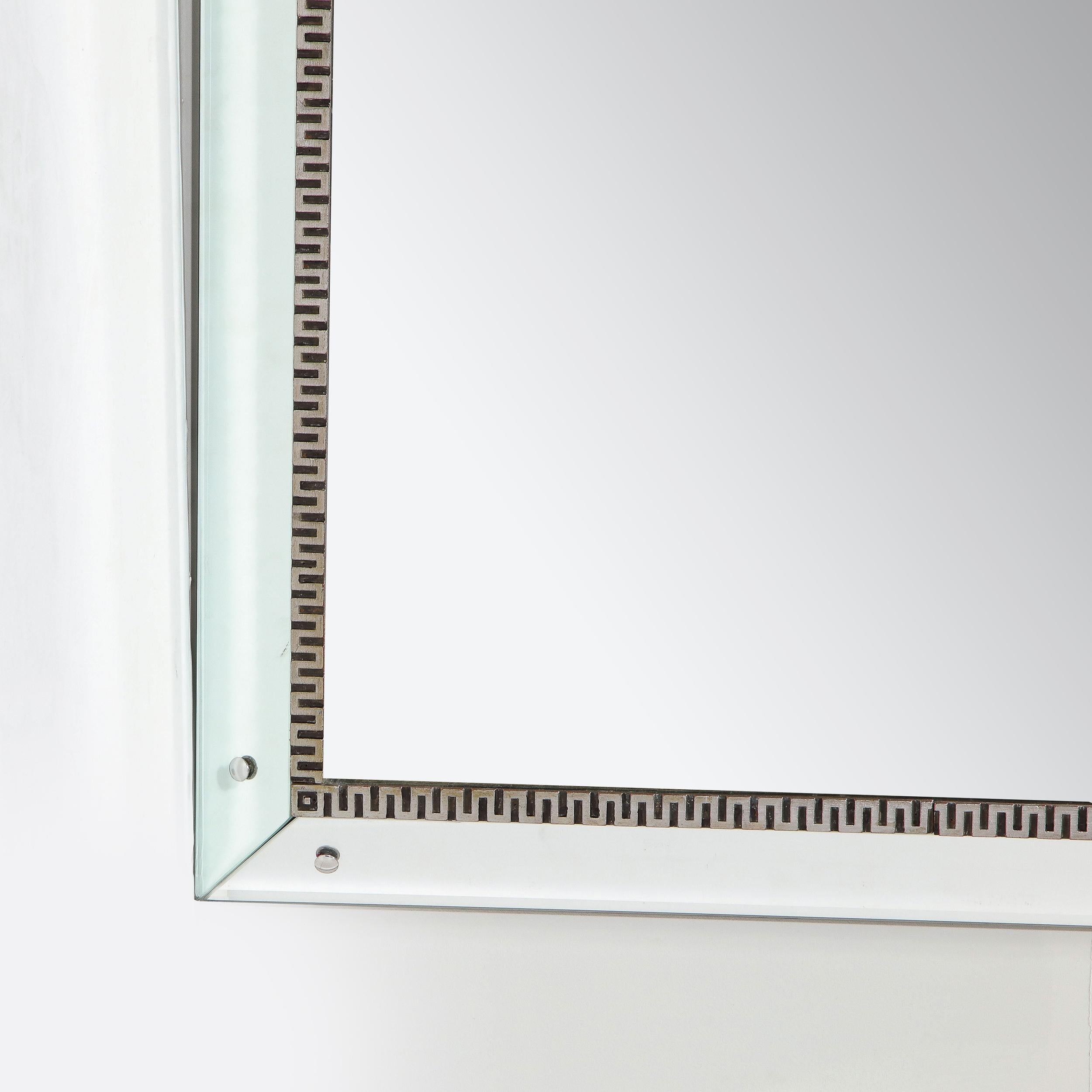 This elegant and understated Mid-Century Modern mirror was realized in the United States, circa 1950. It offers an austere rectangular form with a mirrored border and a plain mirrored center separated by a stylized greek key motif border executed in