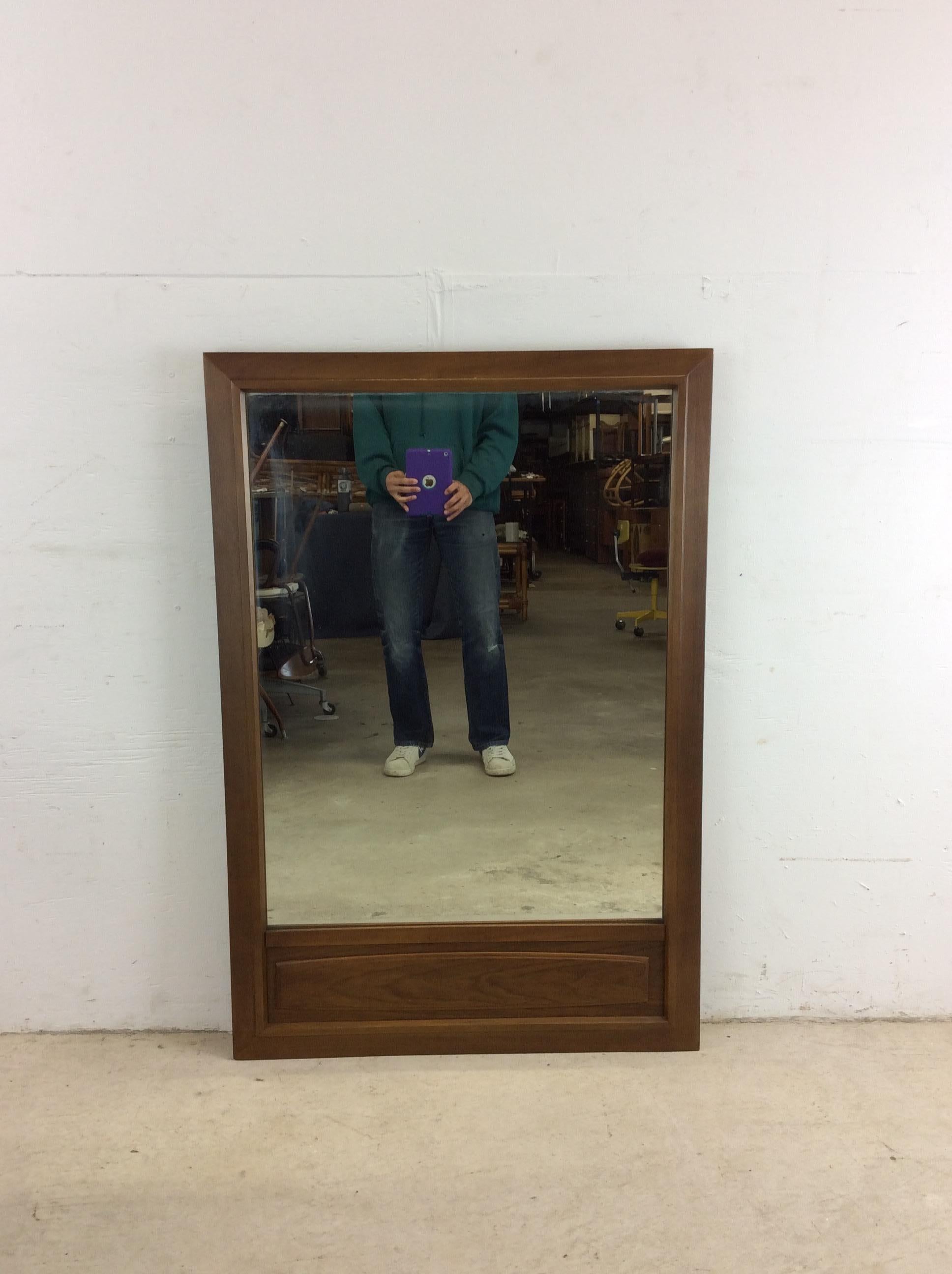 Ce miroir moderne du milieu du siècle présente une construction en bois dur, une finition originale en noyer, un accent unique en noyer à la base et un verre miroir vintage. 
u2028Dimensions : 30.5w 1.5d 44.25h

Condit : La finition d'origine en