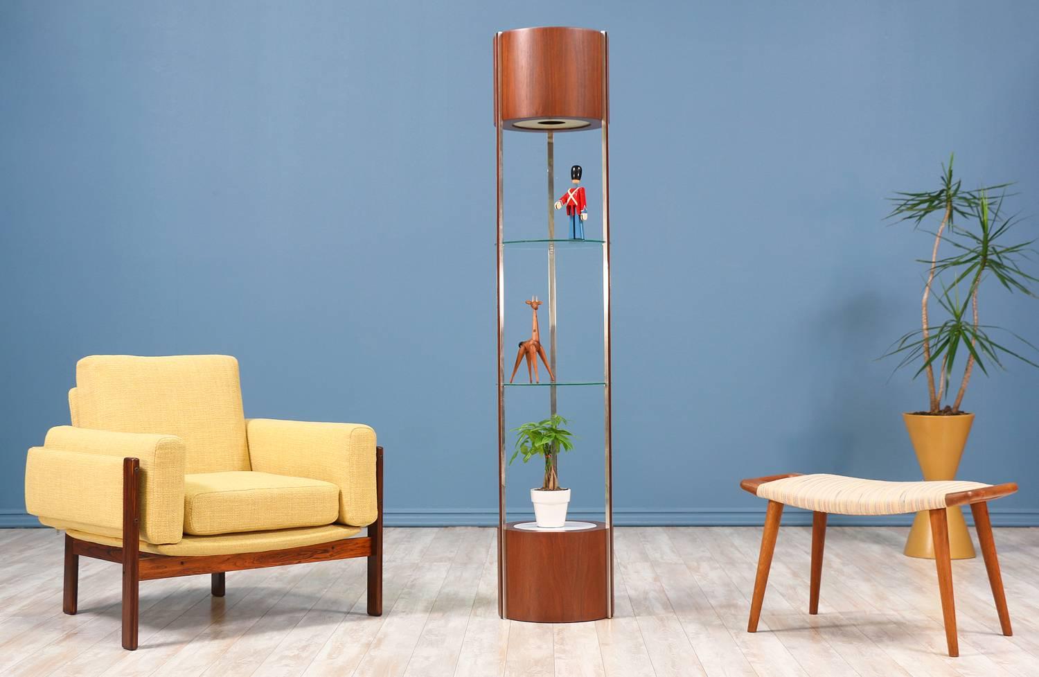 Mid-Century Modern curio cabinet manufactured in the United States circa 1960’s. This cylindrical display case features a solid walnut wood and steel body with plastic light diffusers at the top and bottom for illuminating your collection of