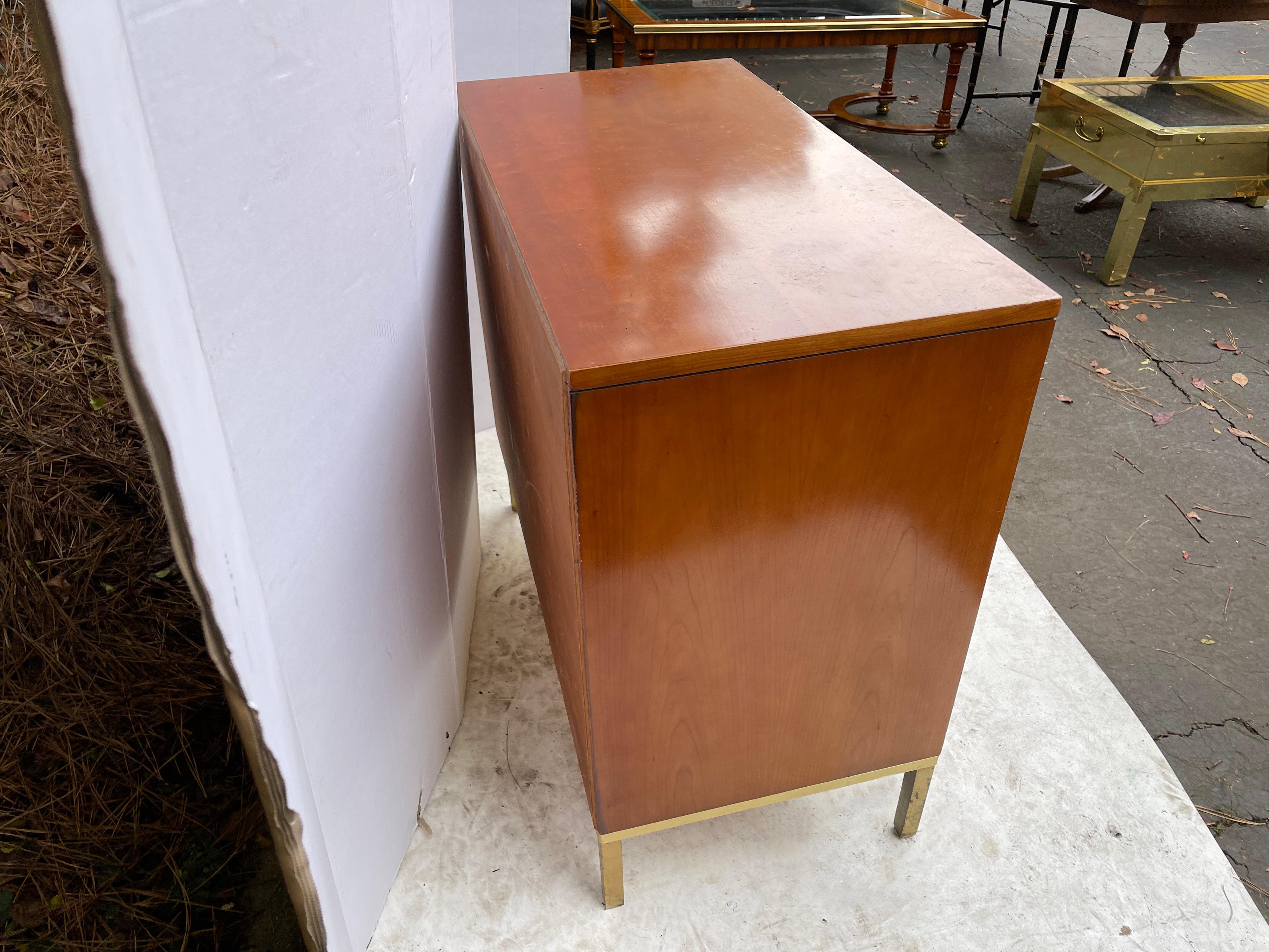 These are a great size with clean lines. This is a pair of midcentury modern walnut on brass based chests by John Stuart. They have three doors. They are marked. The only negative is that the brass is in desperate need of cleaning, which I will give