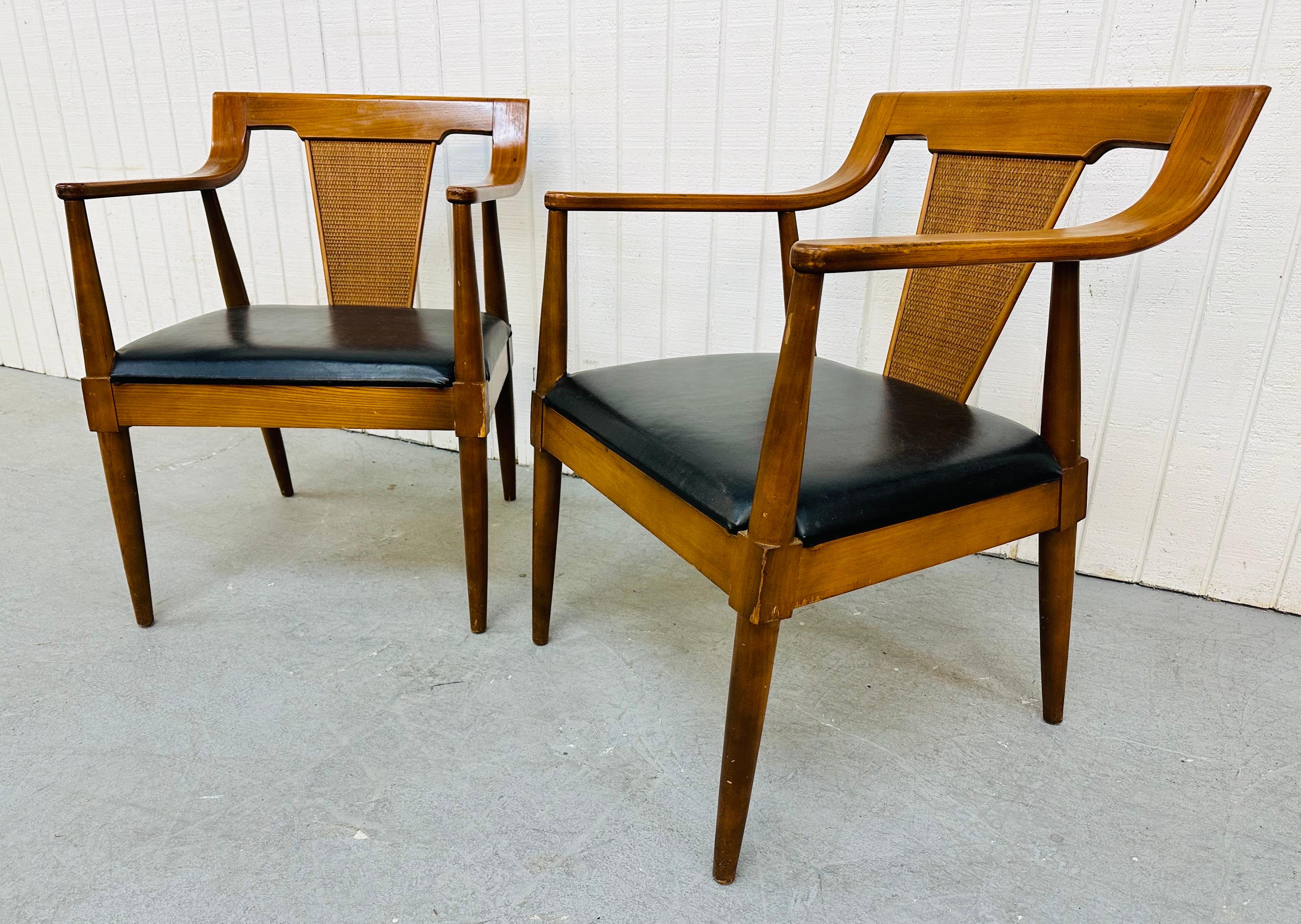 This listing is for a pair of Mid-Century Modern walnut arm chairs. Featuring walnut frames, a cane style back rest, and black vinyl seats.