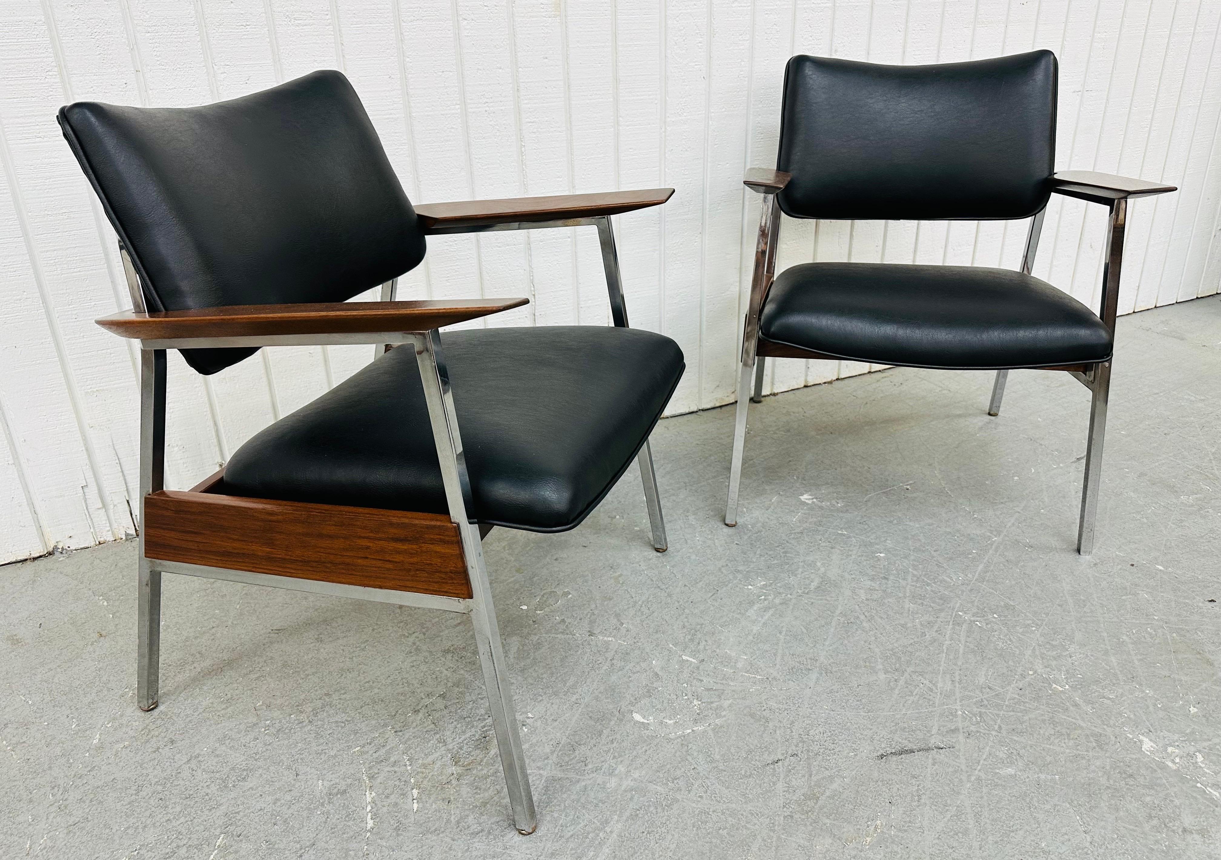 This listing is for a pair of Mid-Century Modern Walnut Arm Chairs. Featuring an industrial style design, chrome frames, black vinyl upholstery, and curved walnut arms that wrap around the back of each chair. This is an exceptional combination of