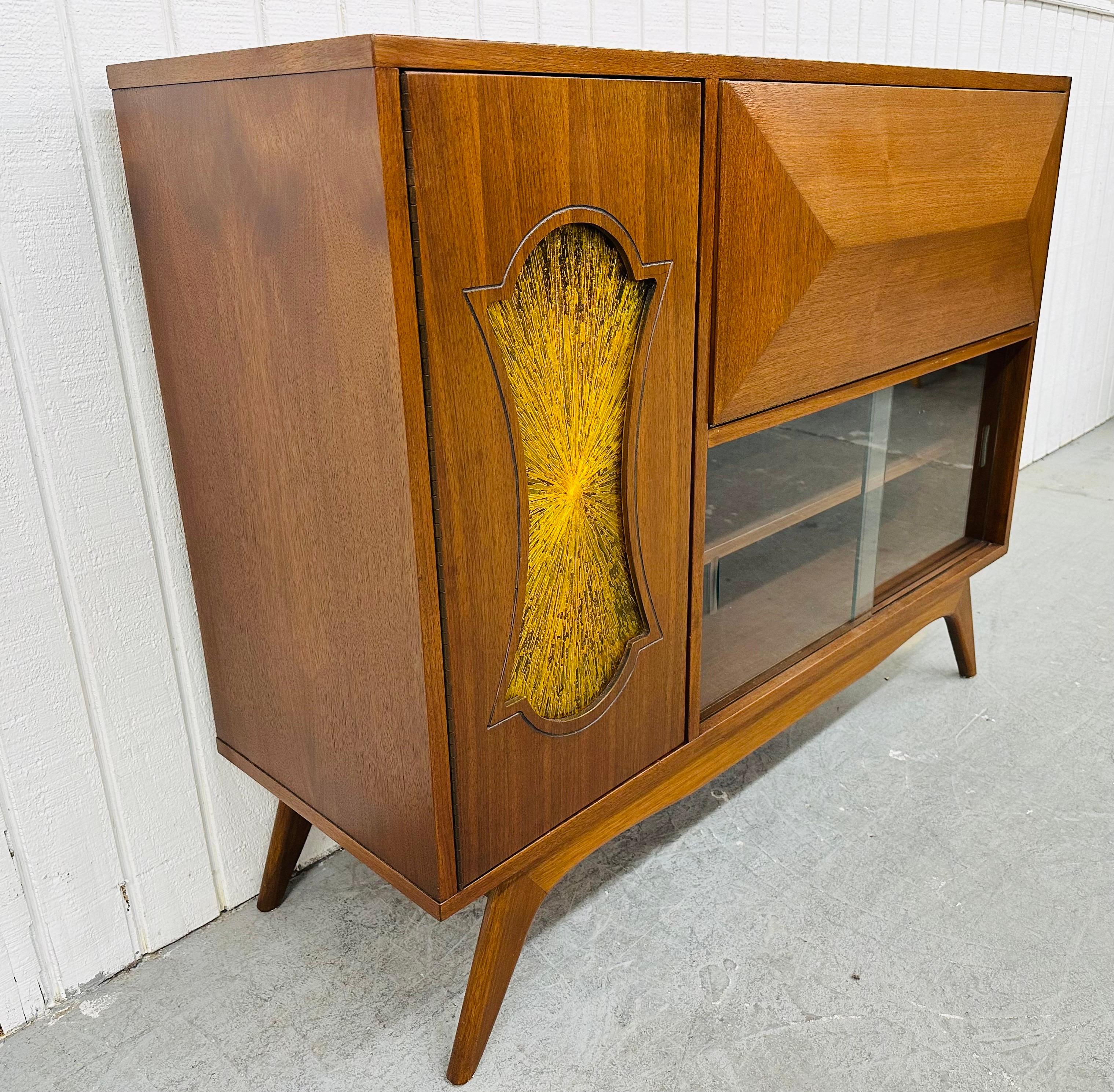 This listing is for a Mid-Century Modern Walnut Bar Cabinet. This super unique piece from the 1960’s features a straight line design, left sided door with yellow stained glass that opens up to storage space, a drop down door that reveals a hidden