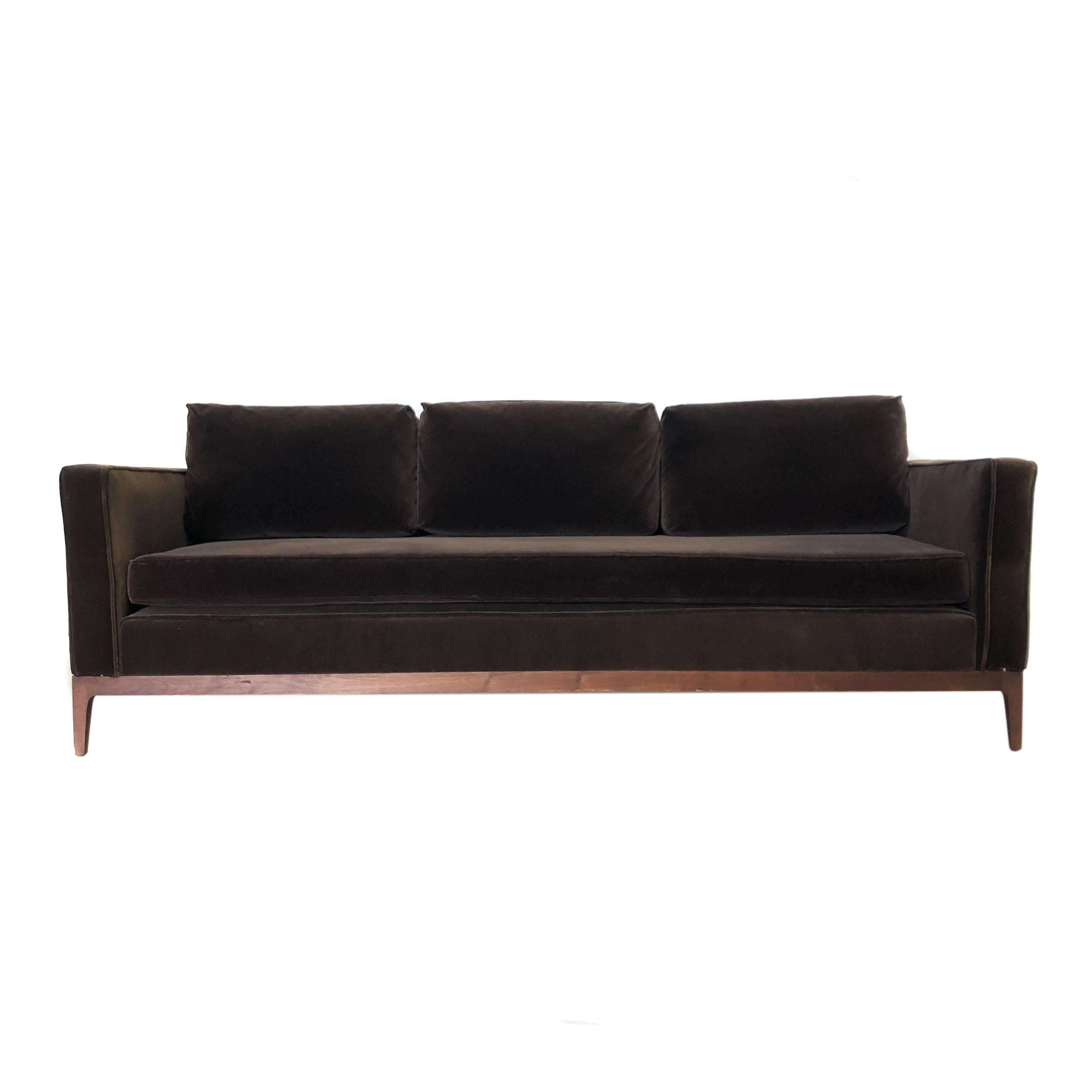 Mid-Century Modern dark brown velvet sofa with a walnut base and legs. Remove the back cushions for deep seating or sleeping. Slight tearing in upholstery on lower corner and sun fading on other arm as seen in photos. Age appropriate